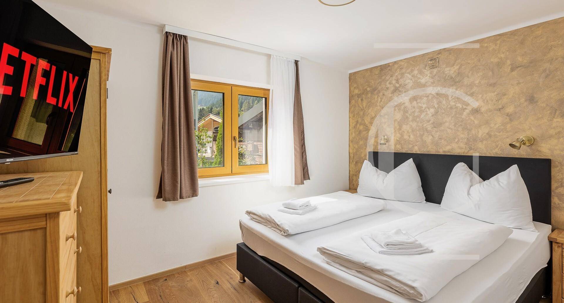 Schlafzimmer mit Doppelbett, Holzboden und einer strukturierten Akzentwand in warmen Farbtönen.