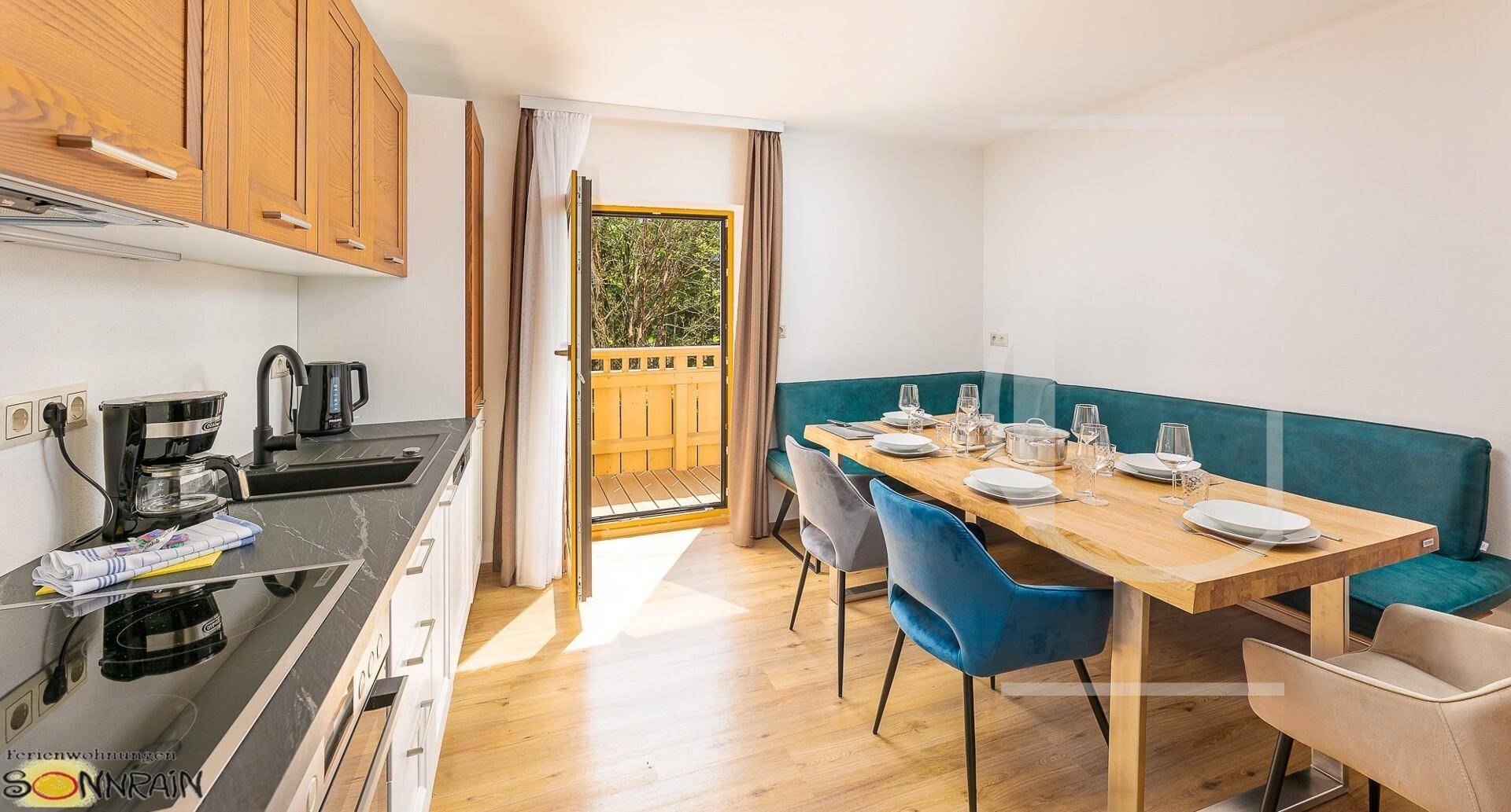 Moderne Küche mit Essbereich und Zugang zum Balkon, ausgestattet mit Holzelementen und blauen Stühlen.