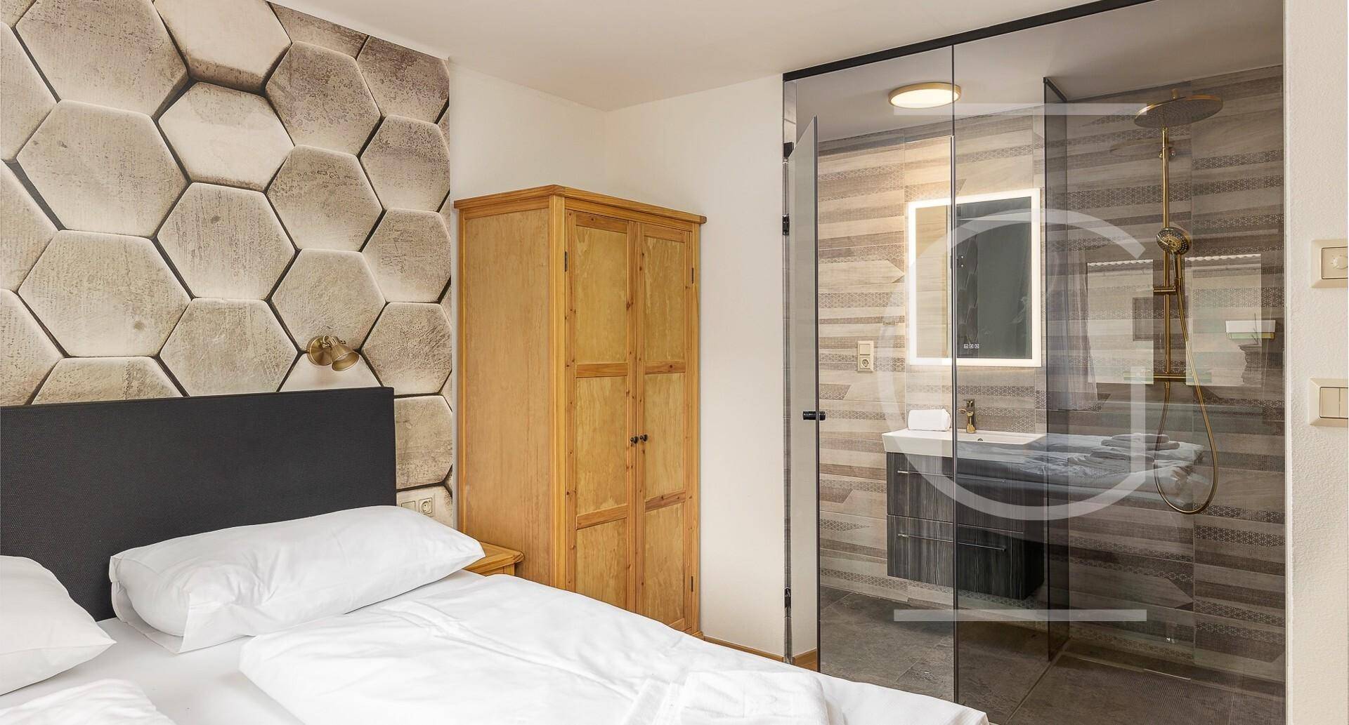 Schlafzimmer mit dekorativer Wand und integrierter Duschkabine, modern gestaltet mit Glasabtrennung.