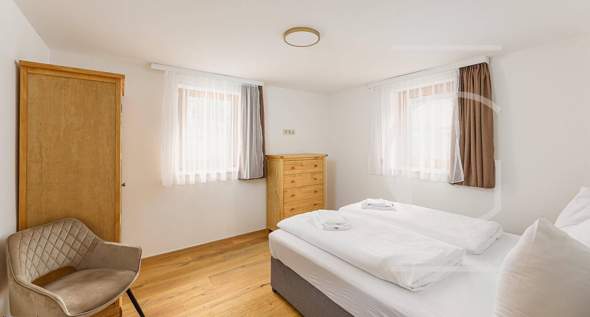 Geräumiges Schlafzimmer mit Doppelbett, Holzmöbeln und zwei Fenstern für viel Tageslicht.