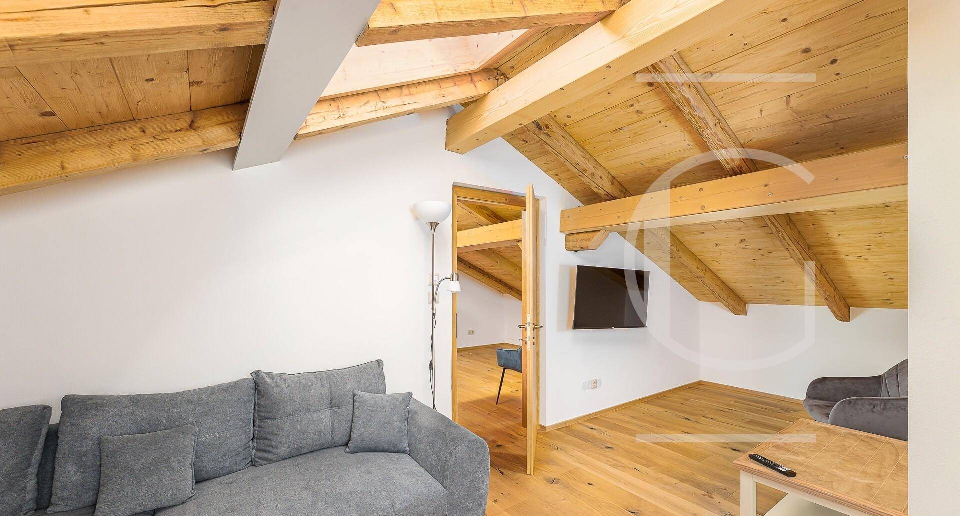 Gemütliches Wohnzimmer im Dachgeschoss mit sichtbaren Holzbalken, Schrägdach und modernem Sofa.