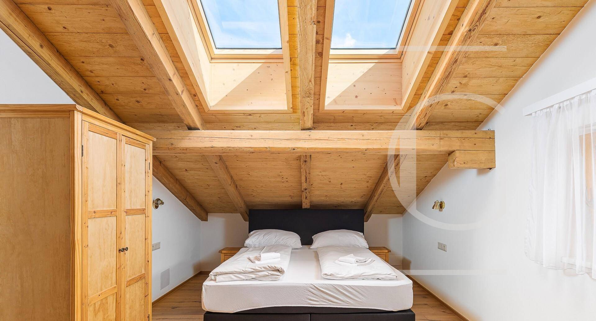 Helles Schlafzimmer im Dachgeschoss mit Holzbalken, Schrägdach und zwei großen Dachfenstern.