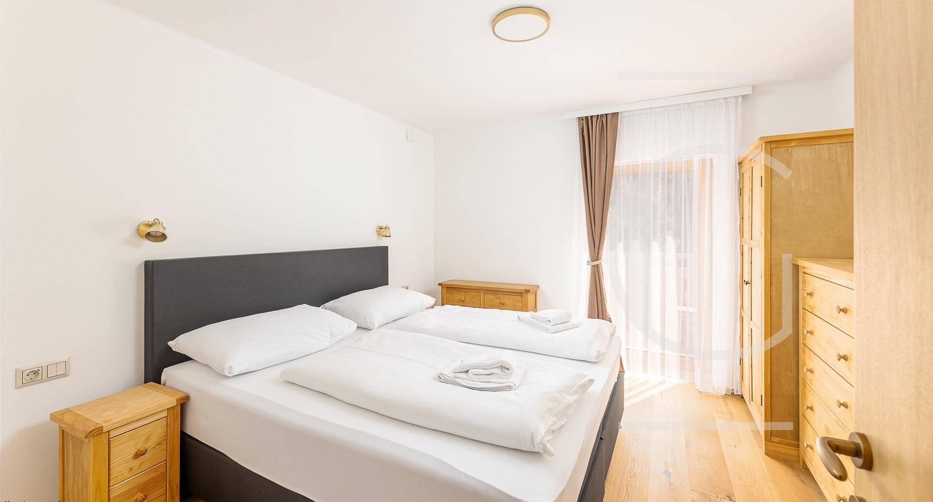 Helles Schlafzimmer mit Doppelbett, Holzmöbeln und Fenster mit Blick ins Grüne.