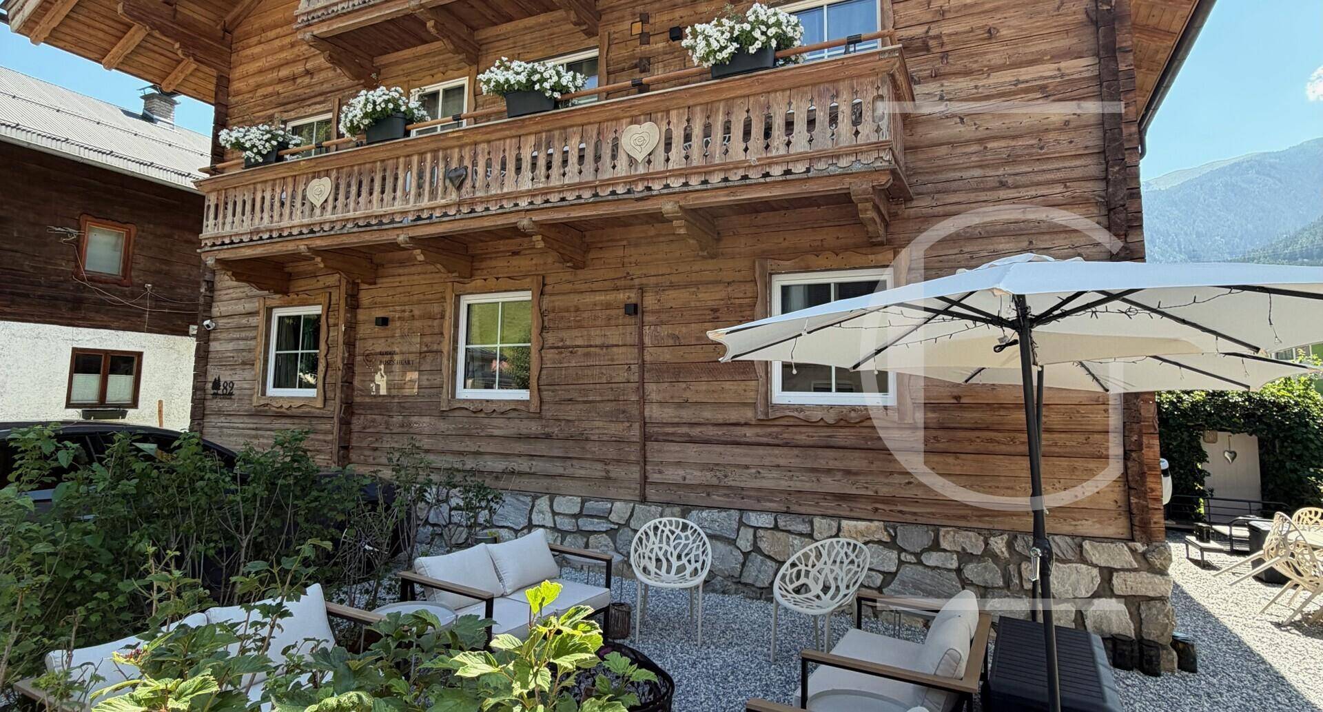 Gemütlicher Gartenbereich mit Sitzgelegenheiten und Sonnenschirm vor einem Holzhaus.