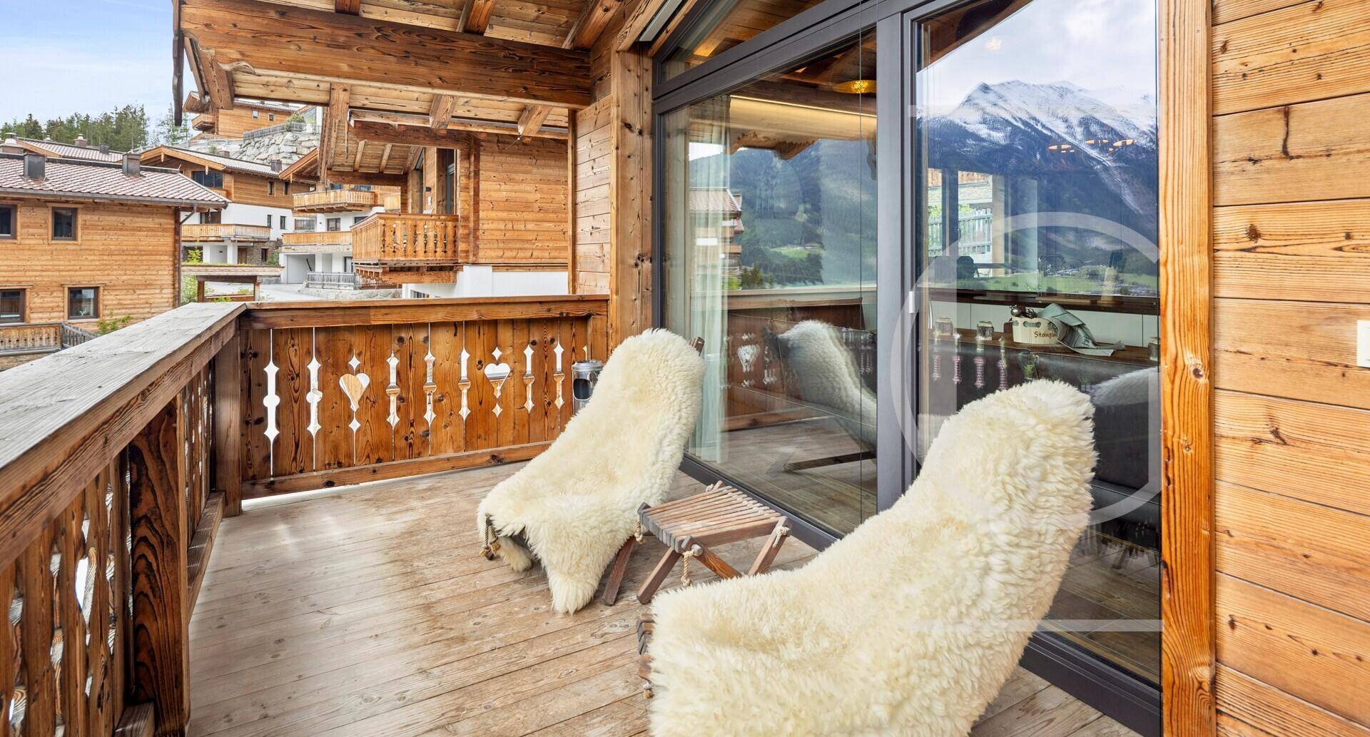 Gemütlicher Balkon mit Schaffell-Sesseln und Panoramablick auf die umliegende Bergwelt.