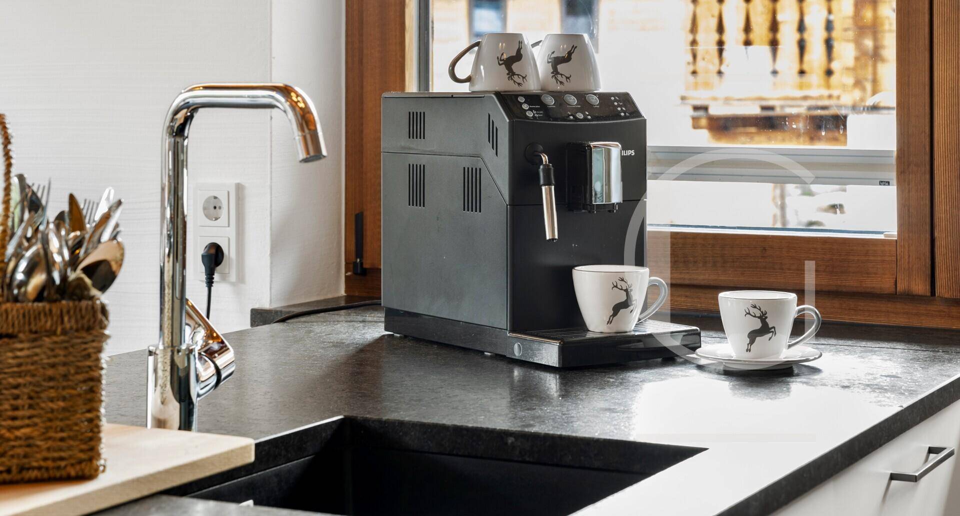 Moderne Kaffeemaschine auf dunkler Arbeitsplatte in einer gut ausgestatteten Küche mit Fenster.