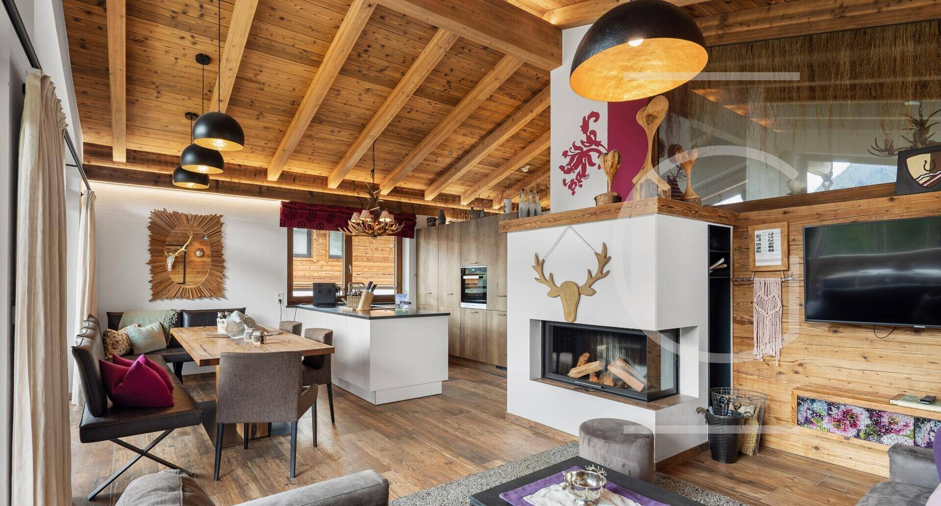 Offener Wohn- und Essbereich mit Holzbalkendecke, Kamin und integrierter Küche im Chalet-Stil.