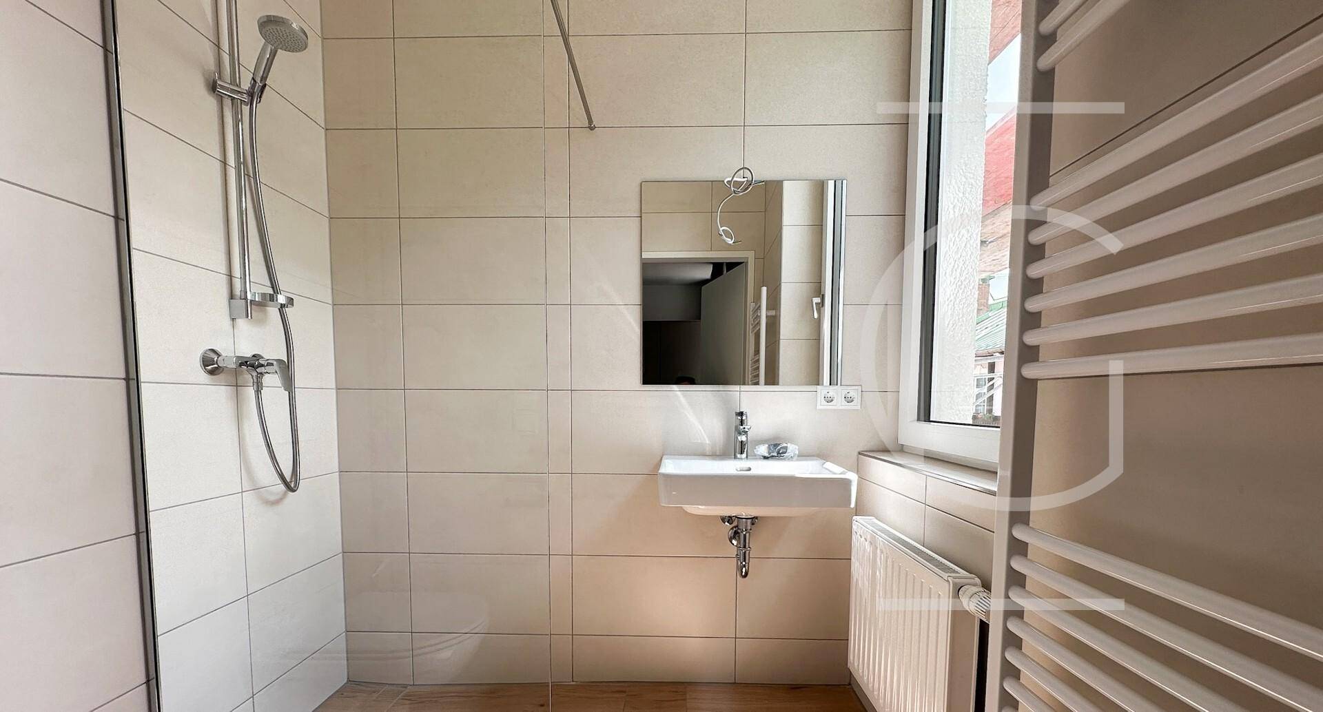 Helles Badezimmer mit Dusche, Waschbecken, Fenster und beheiztem Handtuchhalter.