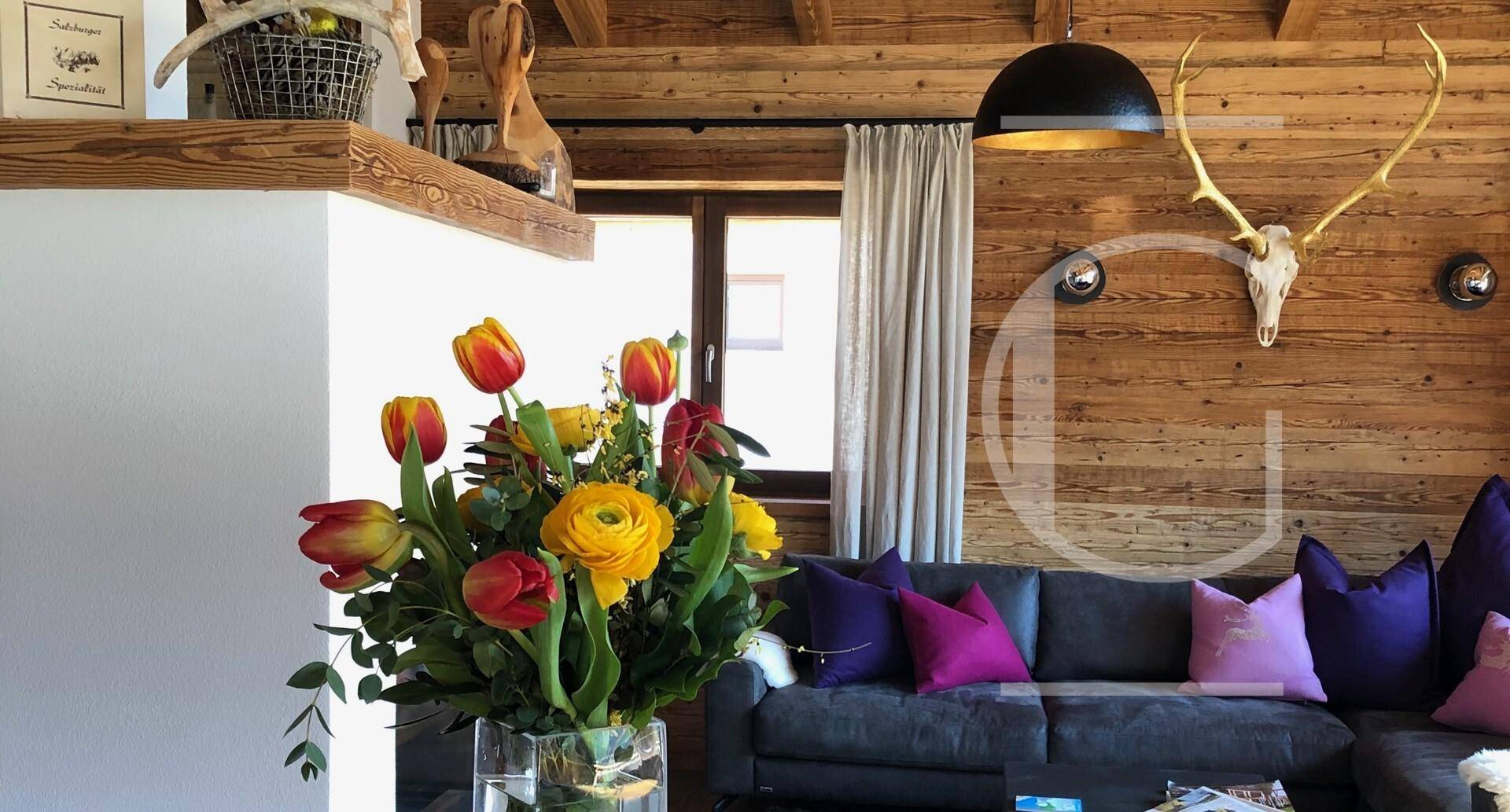 Gemütlicher Wohnbereich im alpinen Stil mit Holzwänden, bequemer Couch und Hirschgeweih-Dekoration.