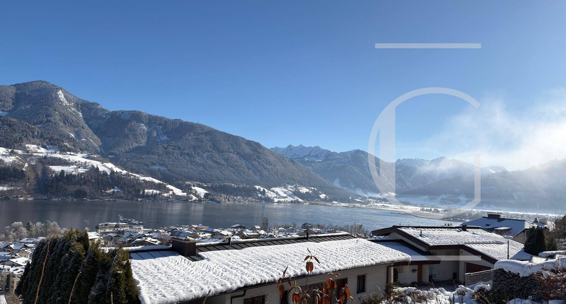 Sonniger Ausblick auf den See und die umliegenden schneebedeckten Berge über den Dächern der Stadt.
