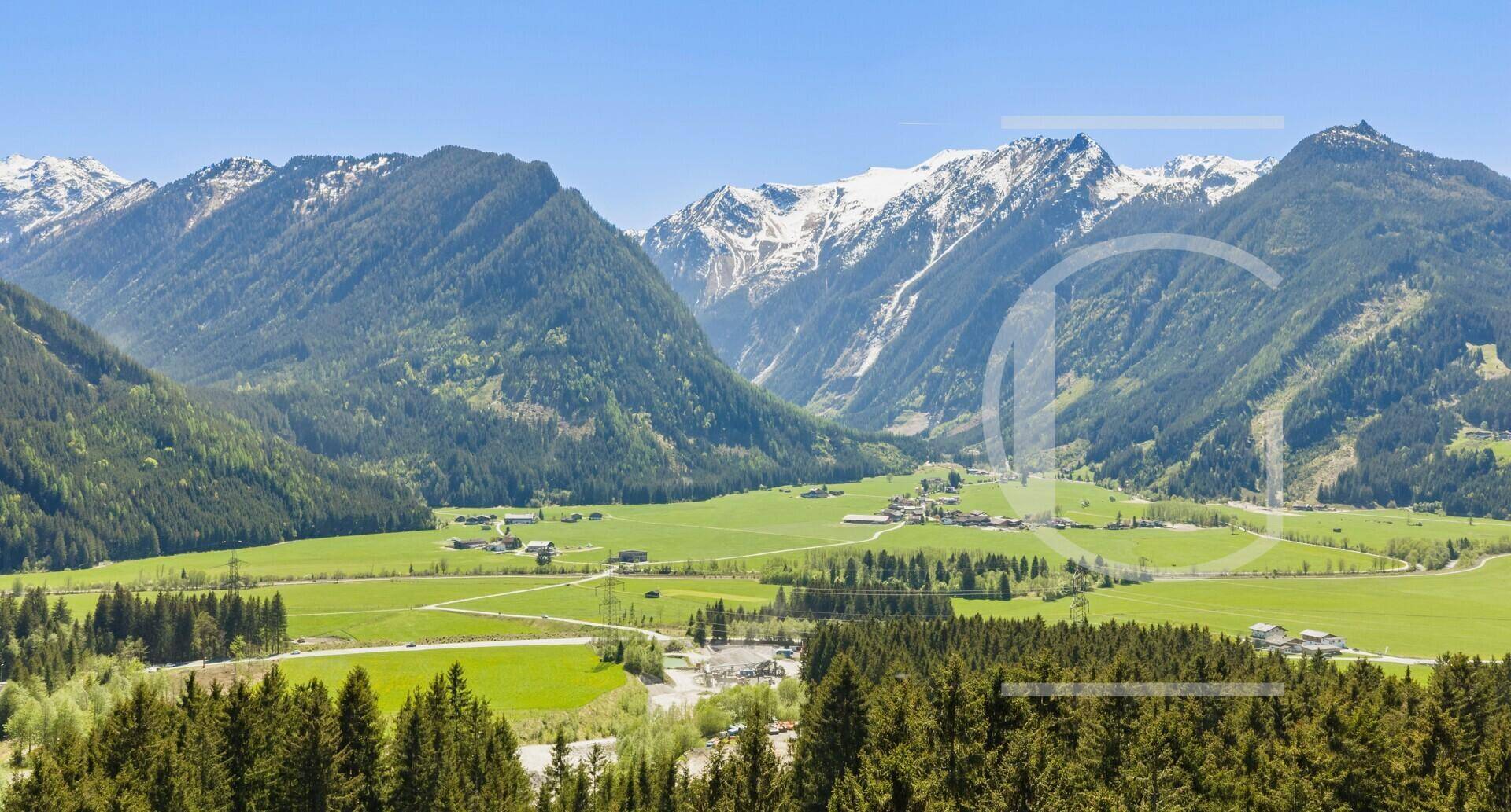 Weitläufige Berglandschaft mit grünen Tälern und schneebedeckten Gipfeln unter blauem Himmel.