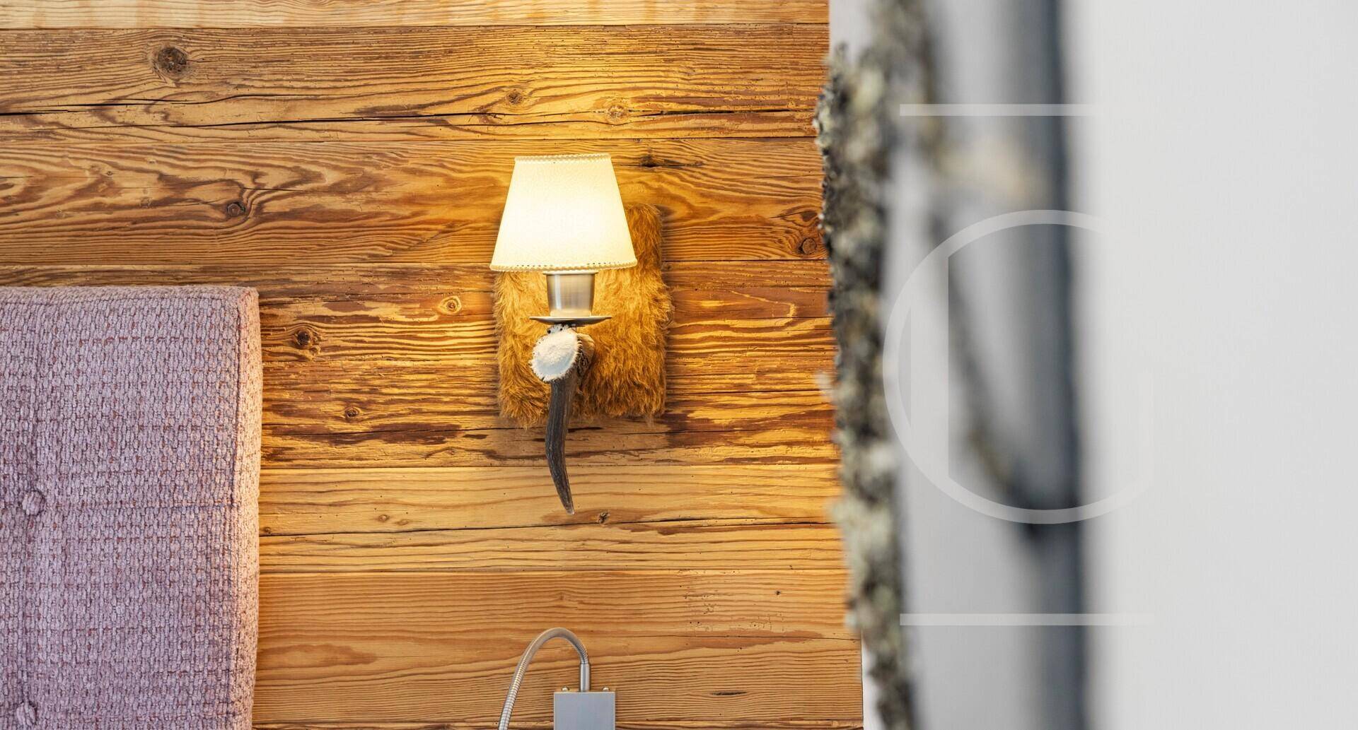Detailaufnahme einer Wandleuchte an einer rustikalen Holzwand im Schlafzimmer.