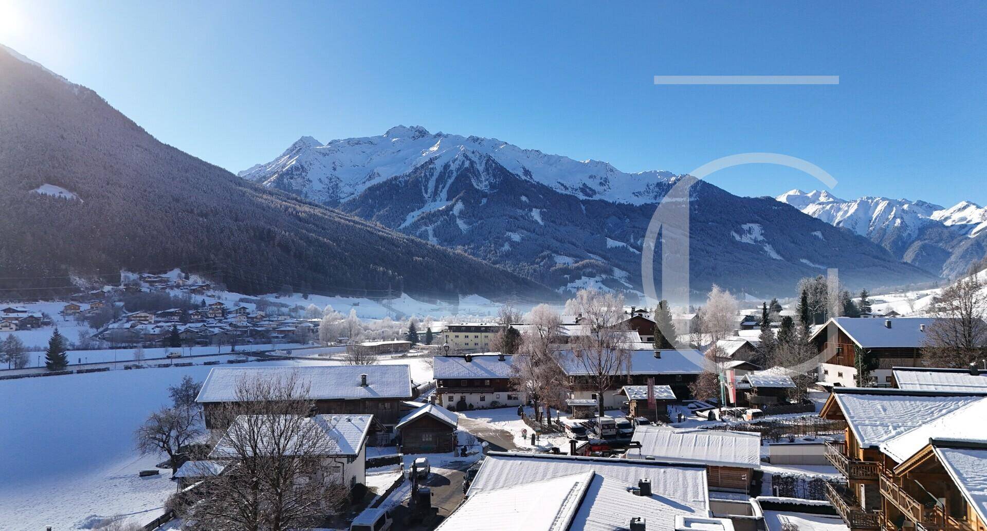 Weitläufiger Blick über ein verschneites Bergdorf mit majestätischen Alpen im Hintergrund.