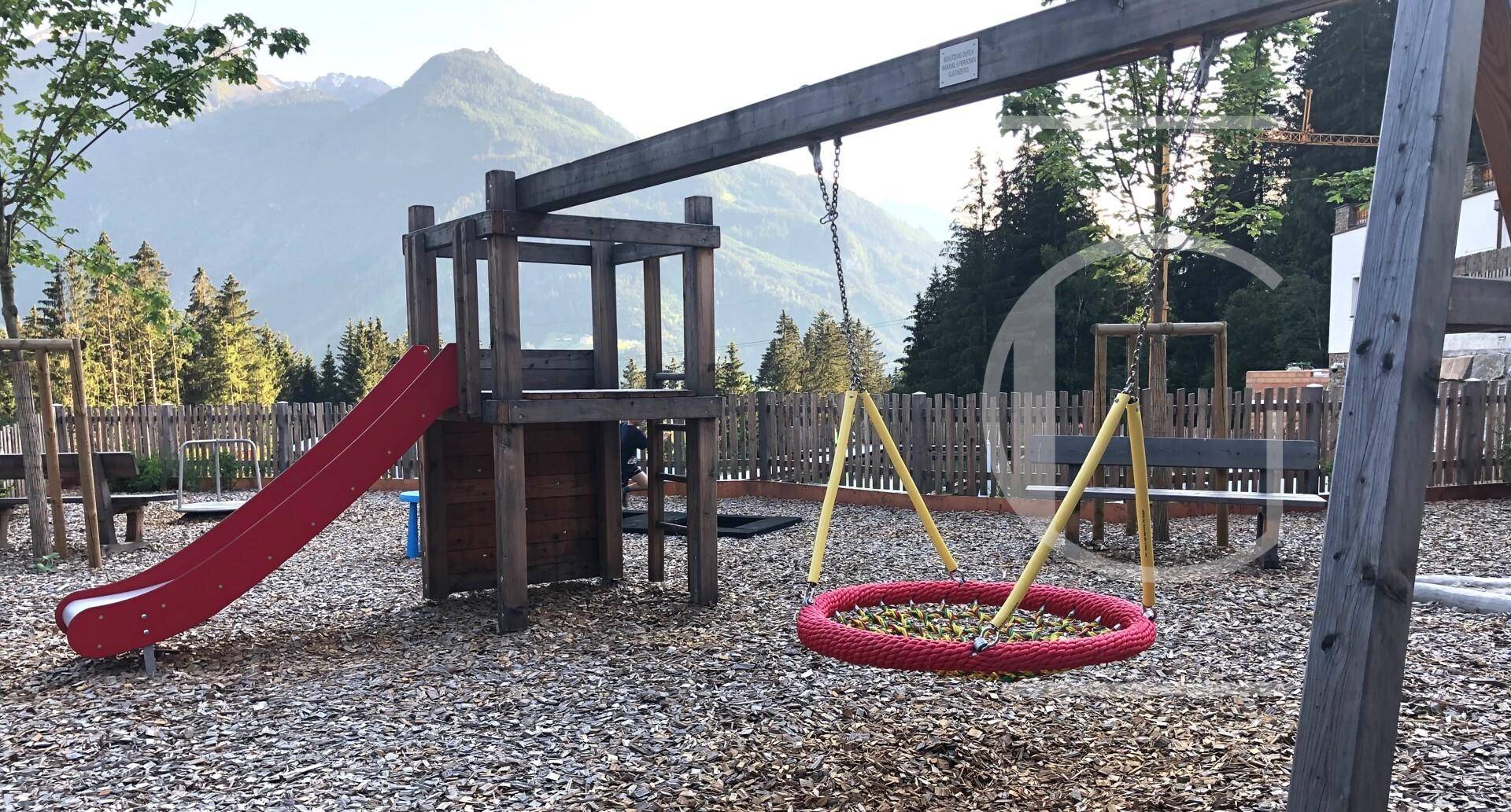 Kinderspielplatz mit Rutsche und Schaukel vor einer malerischen Bergkulisse.
