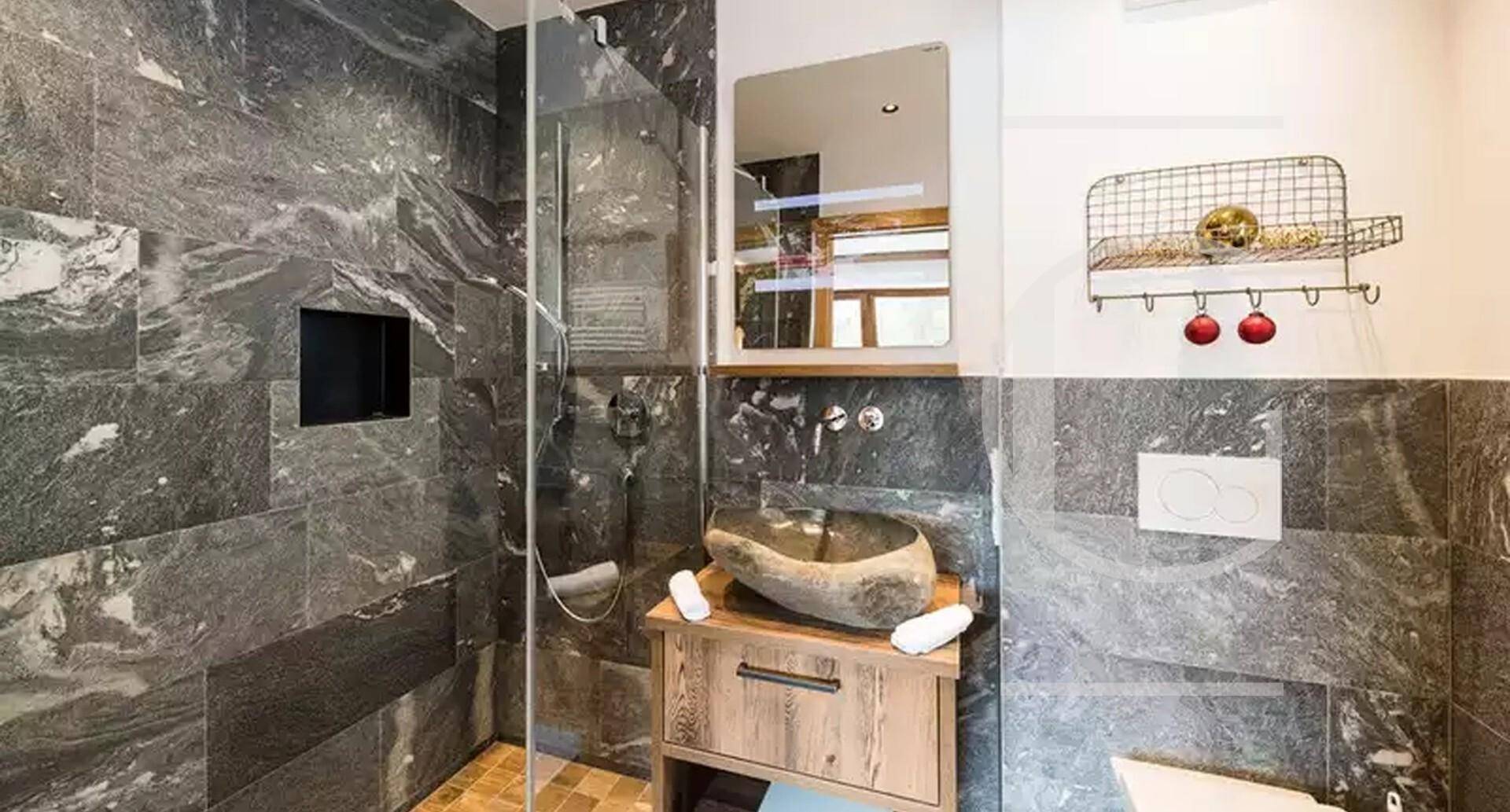 Modernes Badezimmer mit dunklen Steinfliesen, begehbarer Dusche und einzigartigem Steinwaschbecken.