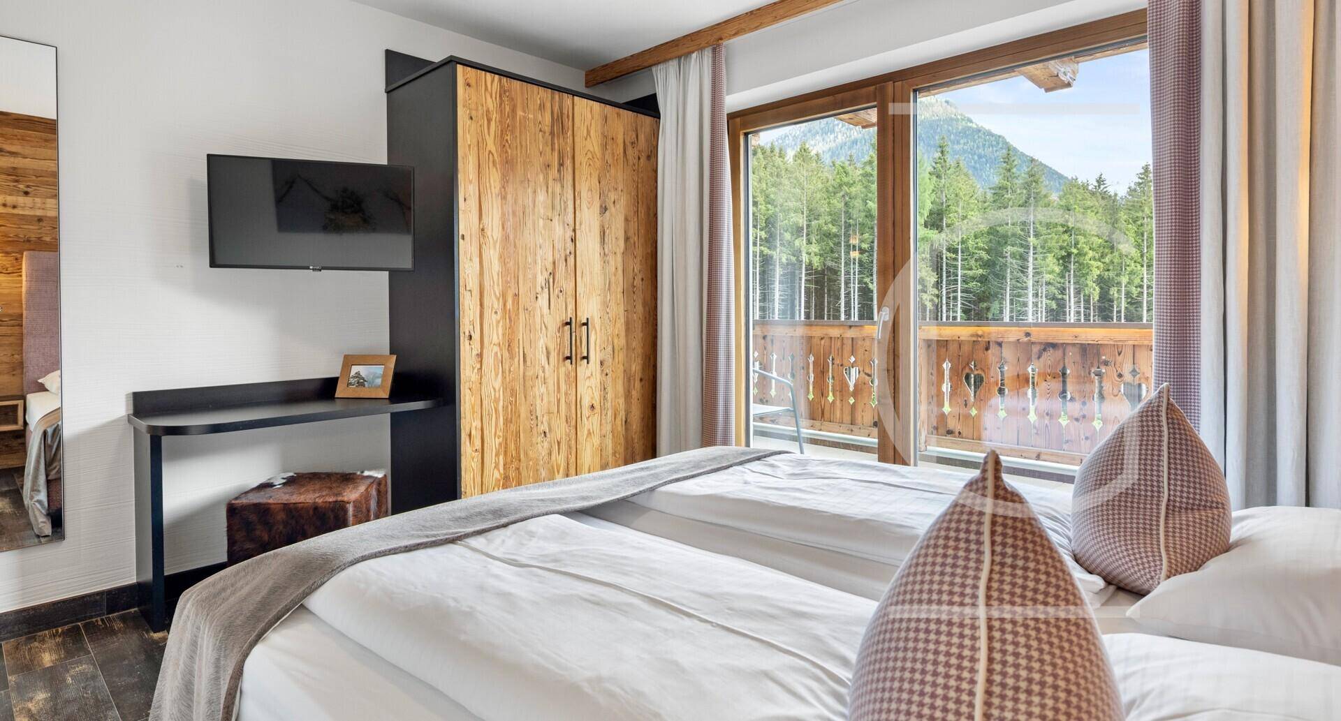 Helles Schlafzimmer mit Holzboden, Kleiderschrank und großen Fenstern mit Bergblick.