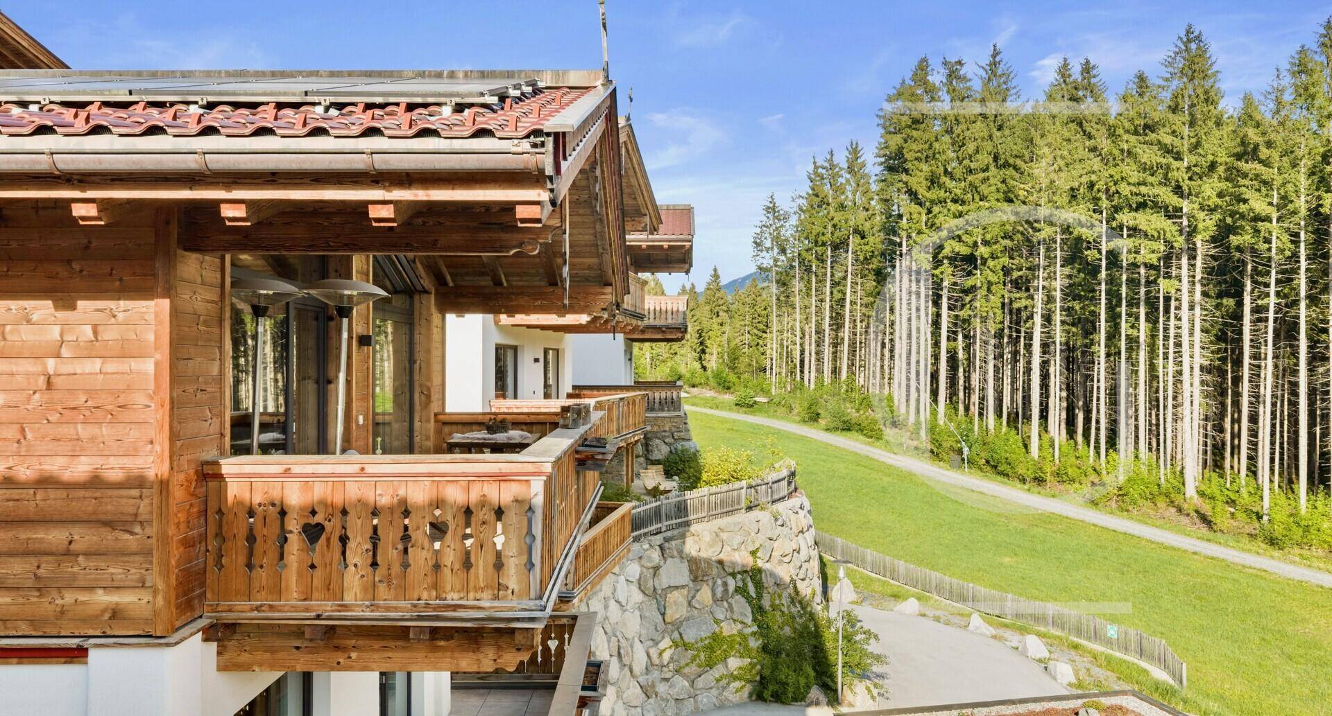 Chalet-Gebäude mit Holzbalkonen und Blick auf den angrenzenden Wald und die Berge.