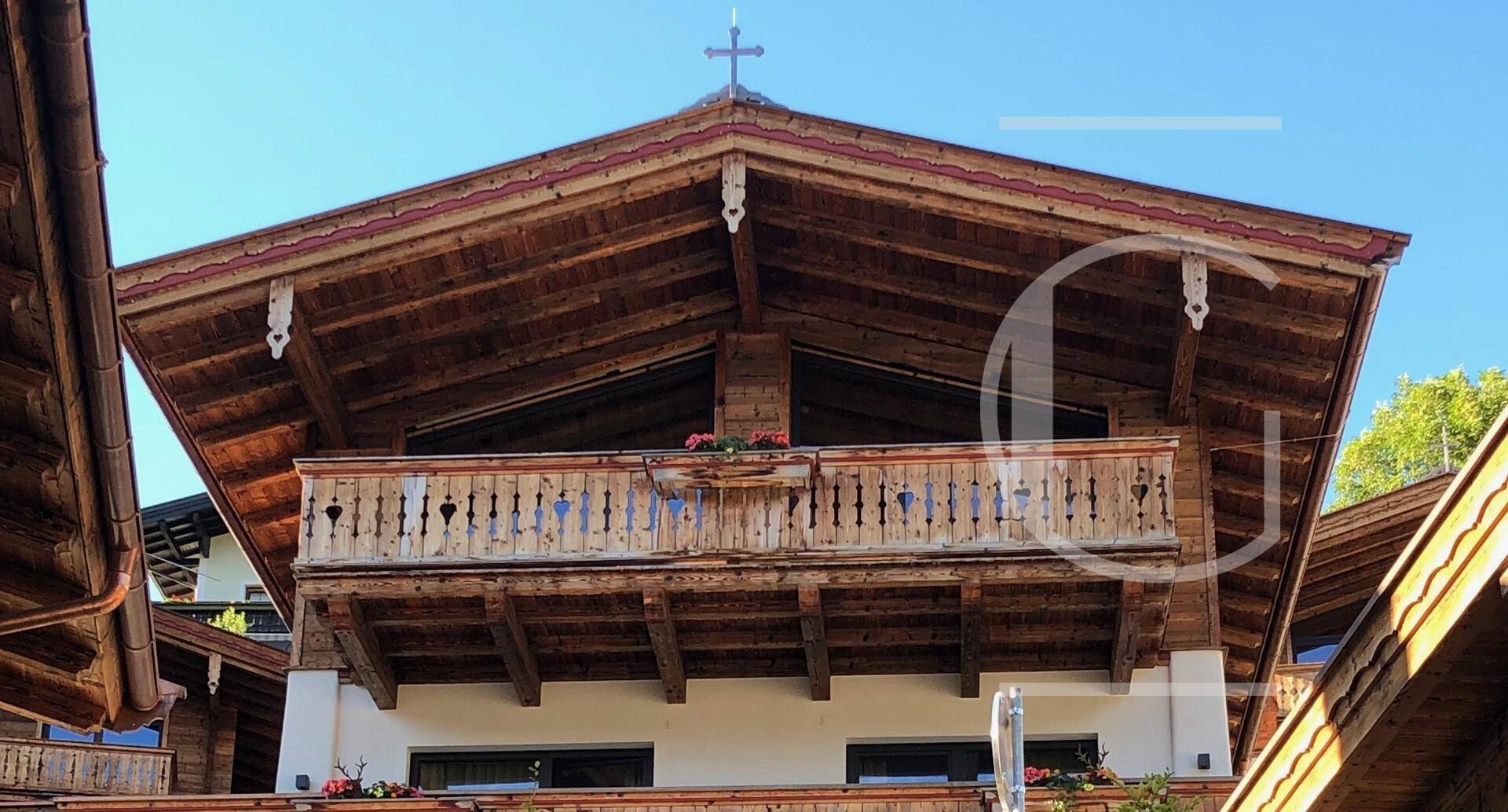 Traditioneller Holzbalkon mit kunstvollen Schnitzereien und Blumenkästen an einem alpinen Gebäude.