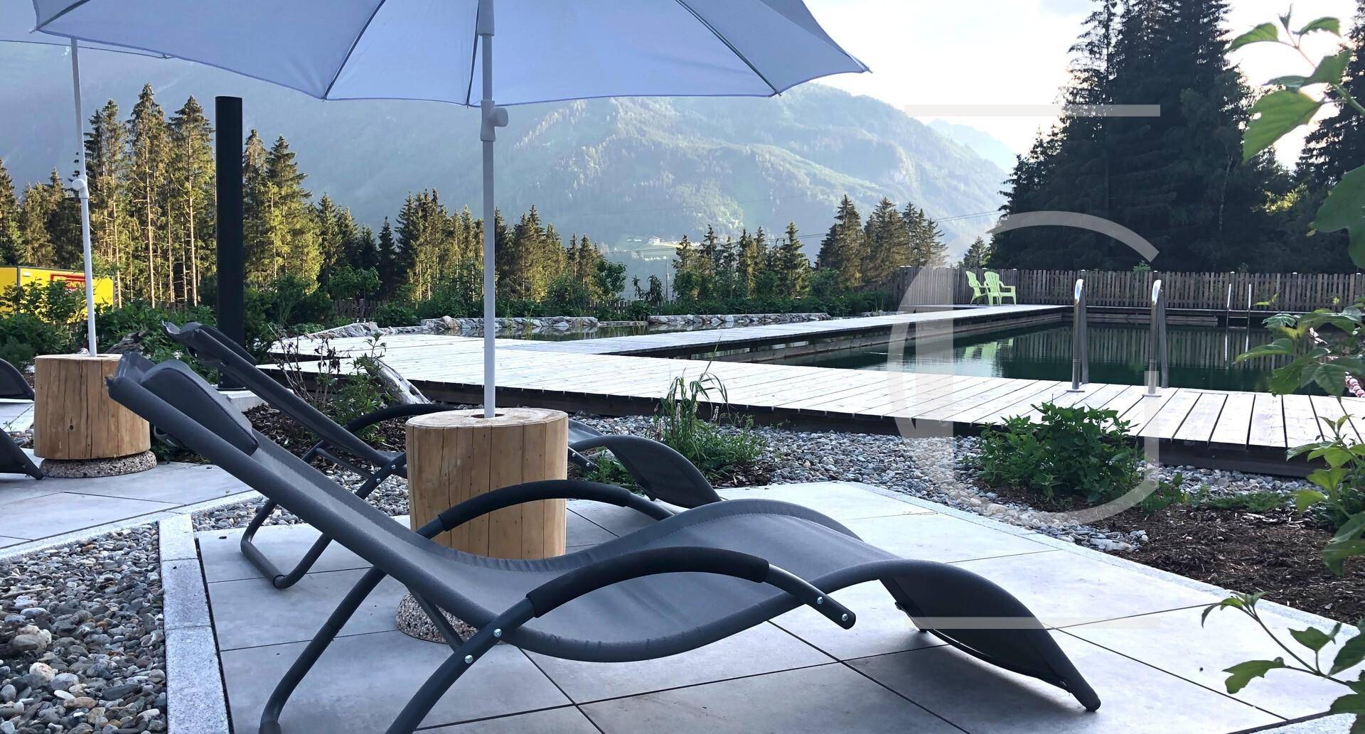Entspannungsbereich am Pool mit Liegestühlen und Blick auf die bewaldeten Berge.