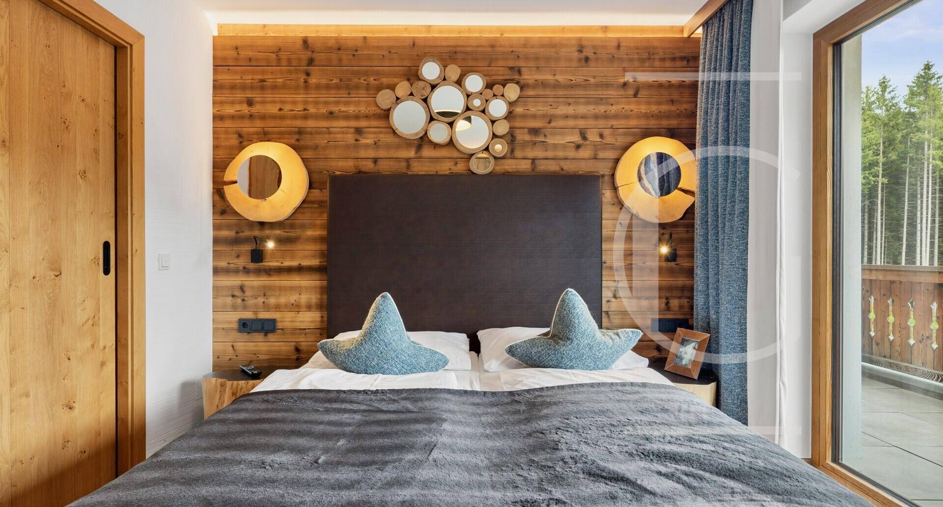 Schlafzimmer im alpinen Stil mit Holzwand, Doppelbett und Zugang zum Balkon mit Bergblick.
