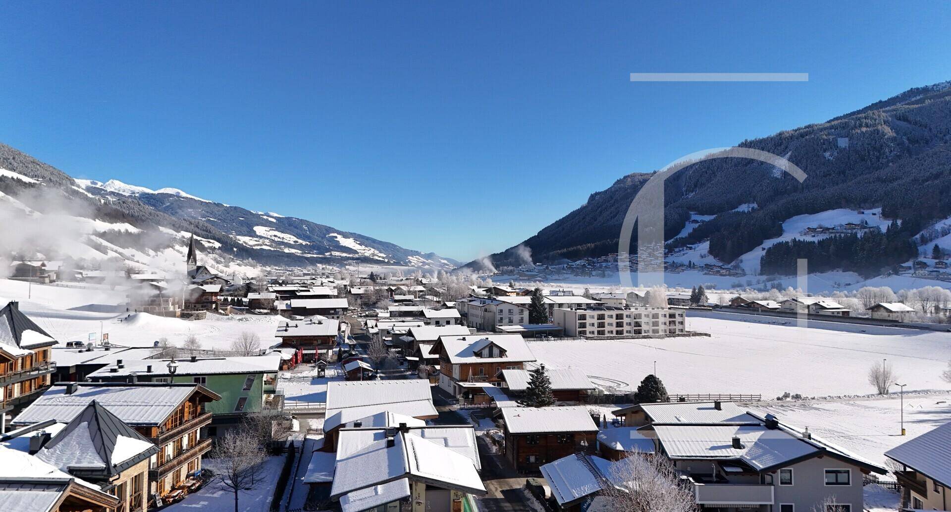 Sonniger Panoramablick auf ein verschneites Tal mit einem charmanten Dorf und Kirche.