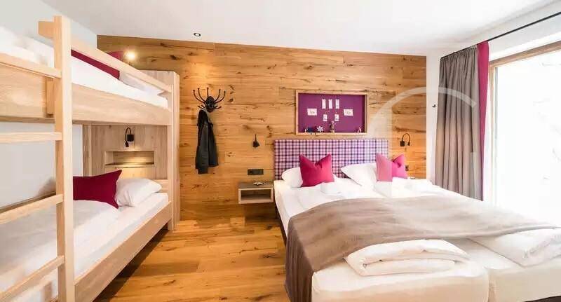 Geräumiges Schlafzimmer mit Doppelbett und Etagenbett, Holzwand und farbigen Akzenten.