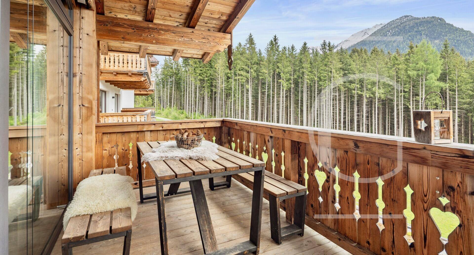Rustikaler Holzbalkon mit Sitzgelegenheiten und Blick auf den Wald und die umliegenden Berge.