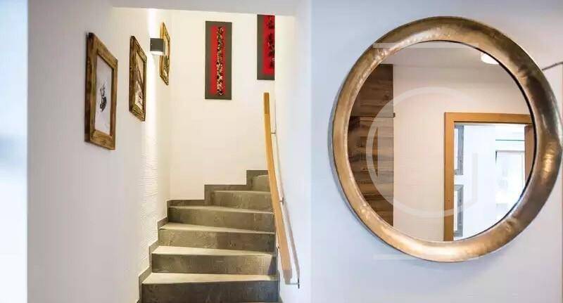 Heller Treppenaufgang mit Holzgeländer und dekorativem Rundspiegel an der Wand.