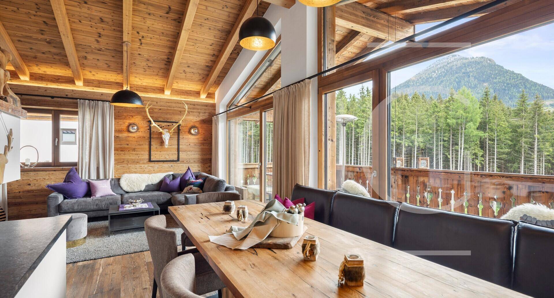 Heller Wohn- und Essbereich mit Holzboden, großen Fenstern und Zugang zu einem Balkon mit Bergblick.