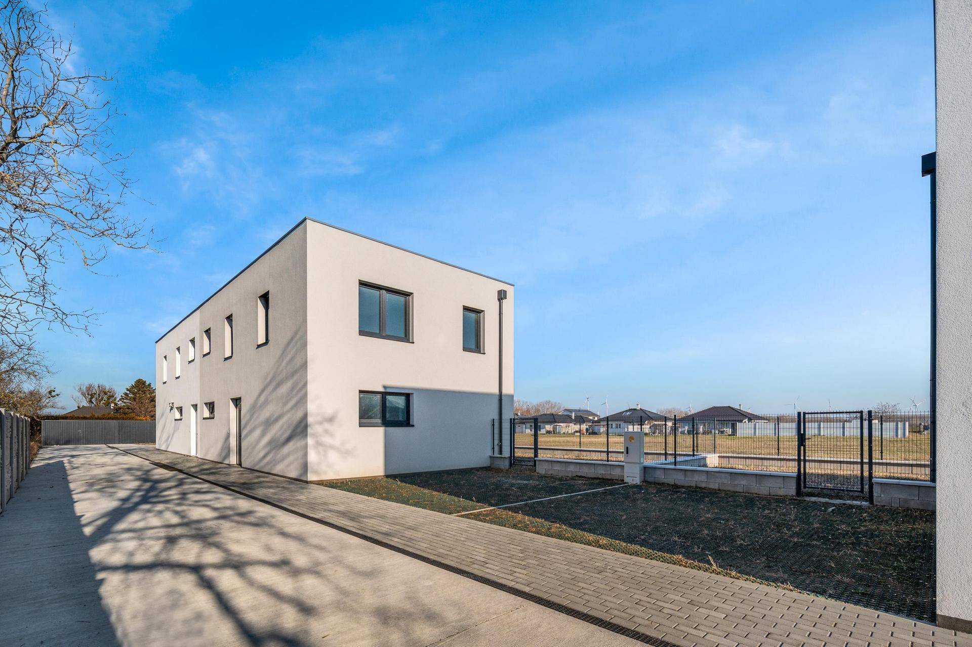 Seitenansicht des modernen Neubaus mit schlichter Fassade und gepflastertem Zugangsbereich.