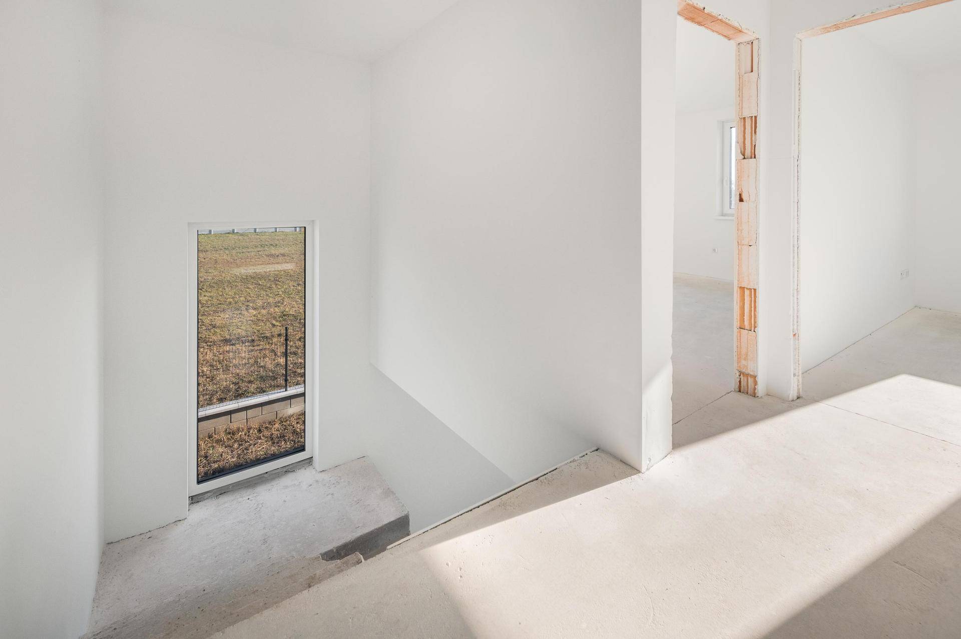Heller Flur mit Treppenabgang und hohem Fenster, das viel Tageslicht hereinlässt.