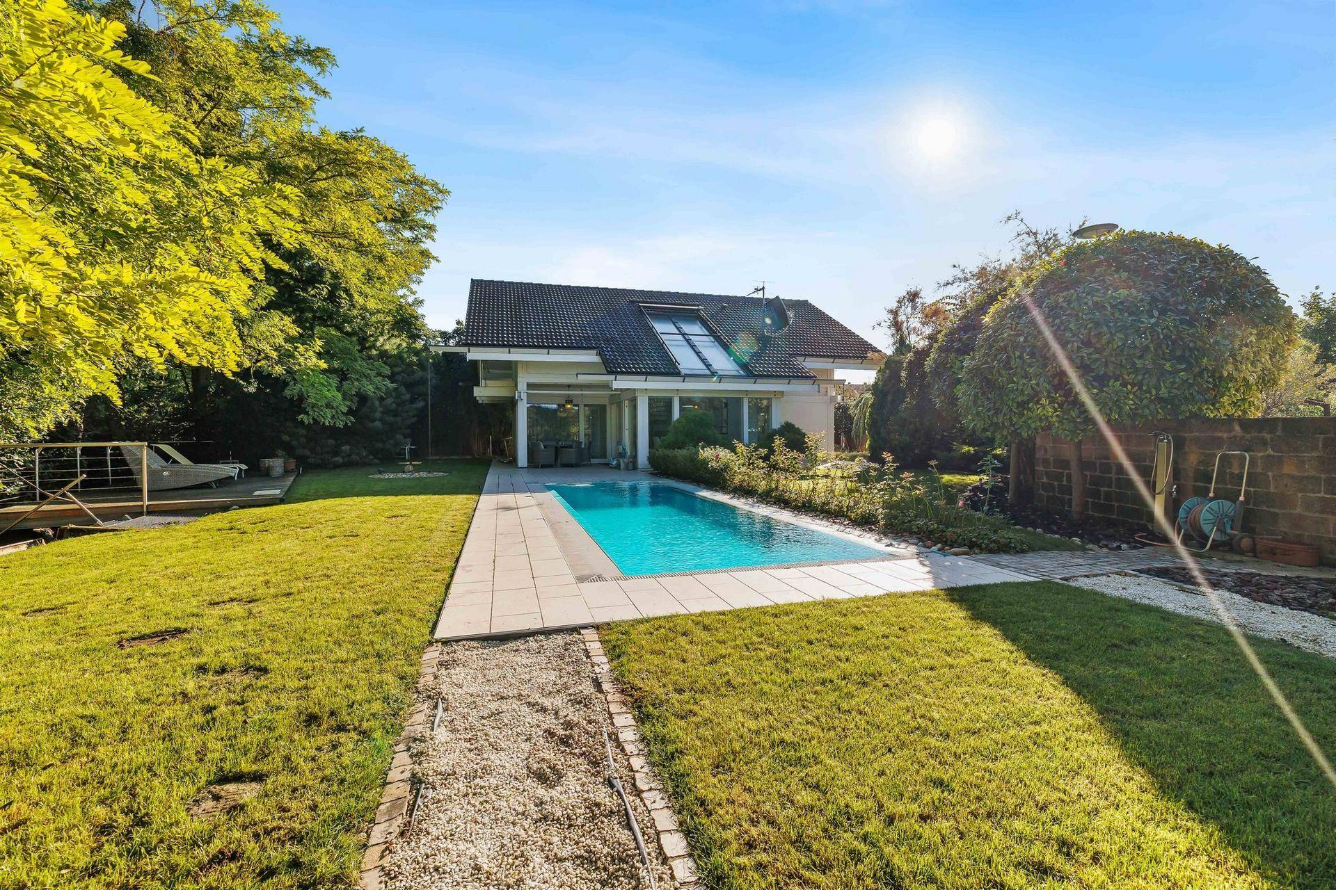 Weitläufiger Garten mit Pool, Rasenflächen und Kiesweg, umgeben von üppiger Vegetation.