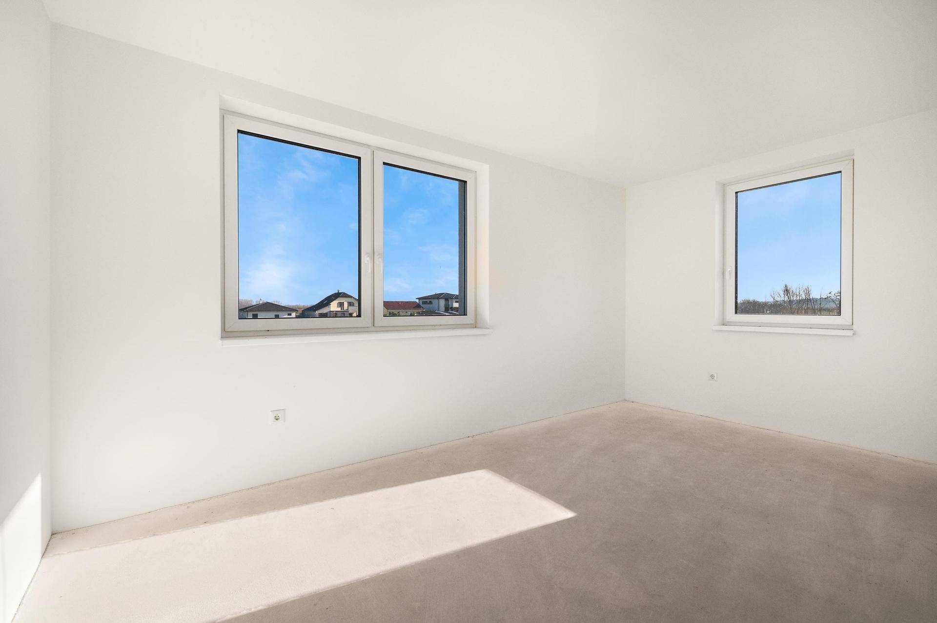 Unmöbliertes Zimmer mit zwei Fenstern, die einen Blick auf die umliegenden Häuser bieten.