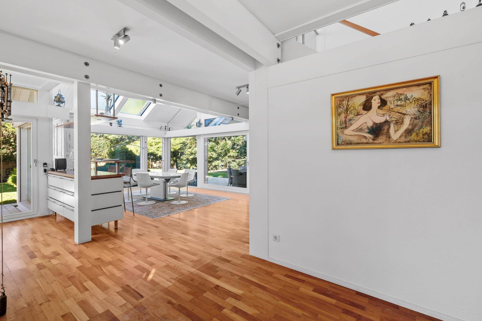 Offener Wohn- und Essbereich mit Holzboden, Blick auf die Küche und Kunst an der Wand.