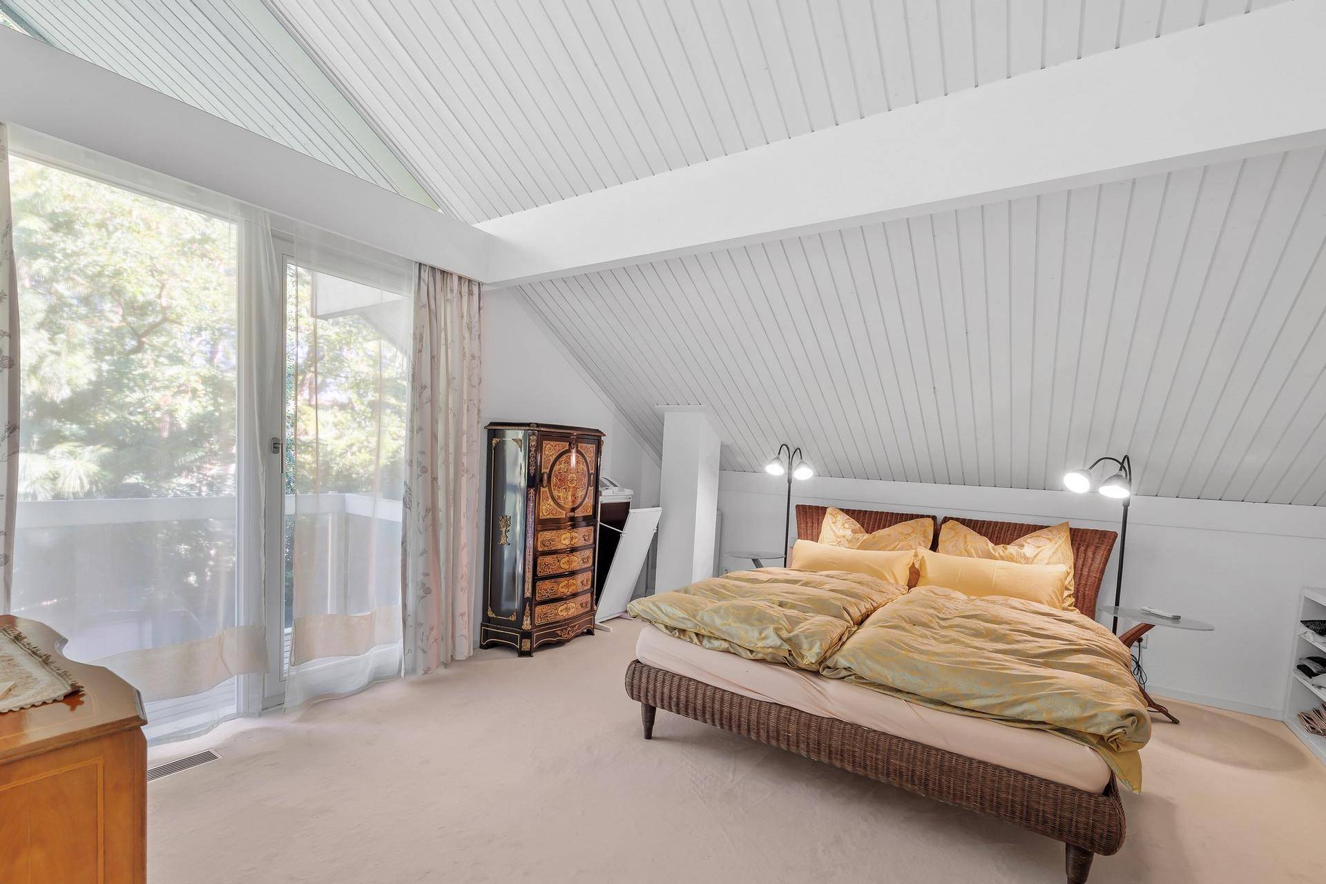Gemütliches Schlafzimmer im Dachgeschoss mit schrägen Decken, großen Fenstern und Balkonzugang.