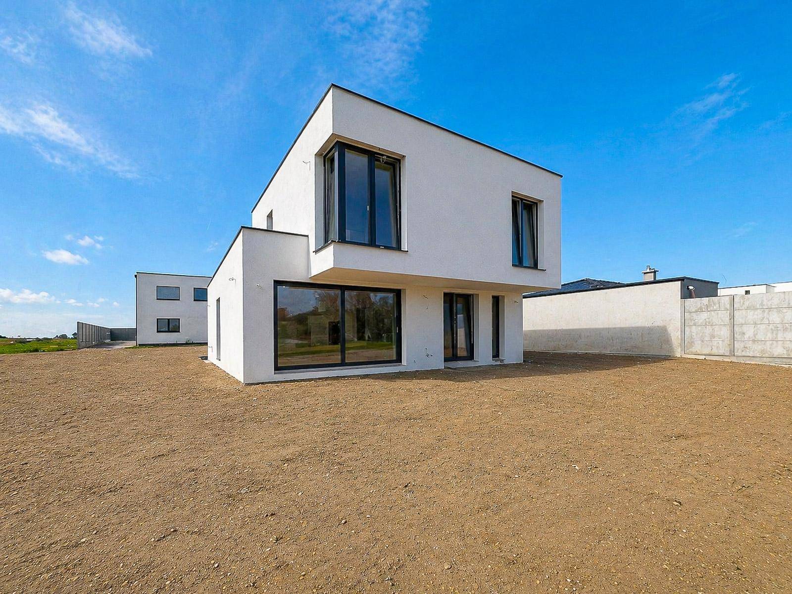 Seitenansicht des modernen Neubaus mit großen Fensterfronten und vorbereitetem Gartenbereich.