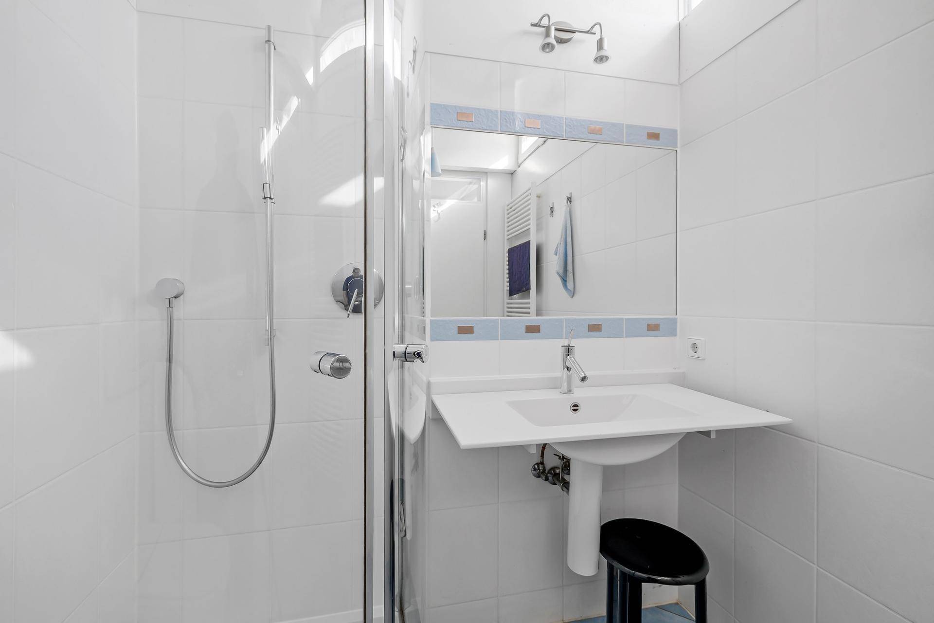 Kleines Badezimmer mit Duschkabine, weiß gefliest und einem einzelnen Waschbecken.