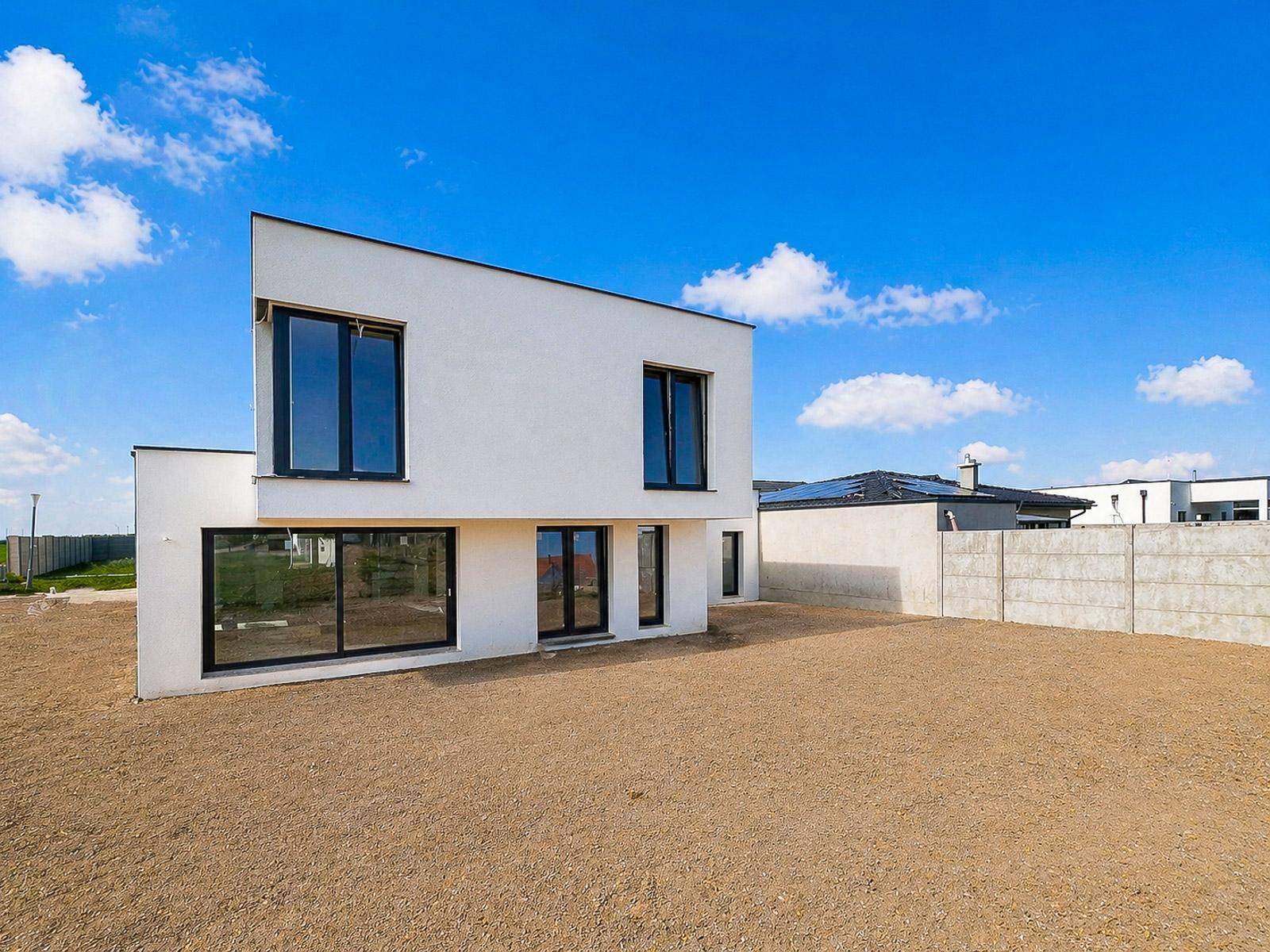 Seitenansicht des modernen Neubaus mit großen Fenstern und einer Betonmauer im Hintergrund.