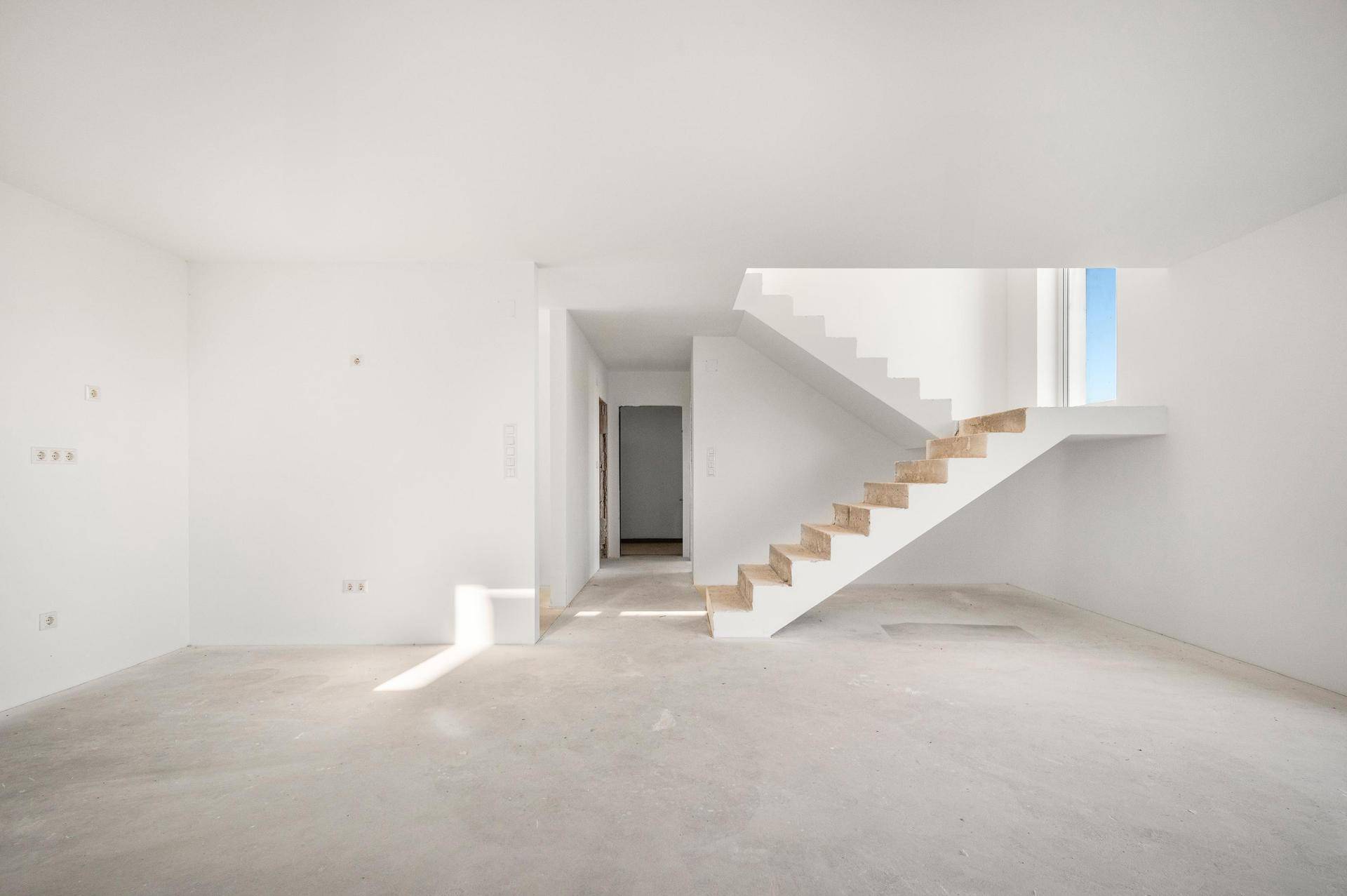 Heller, unmöblierter Raum mit weiß gestrichenen Wänden und moderner Treppe mit Holzstufen.