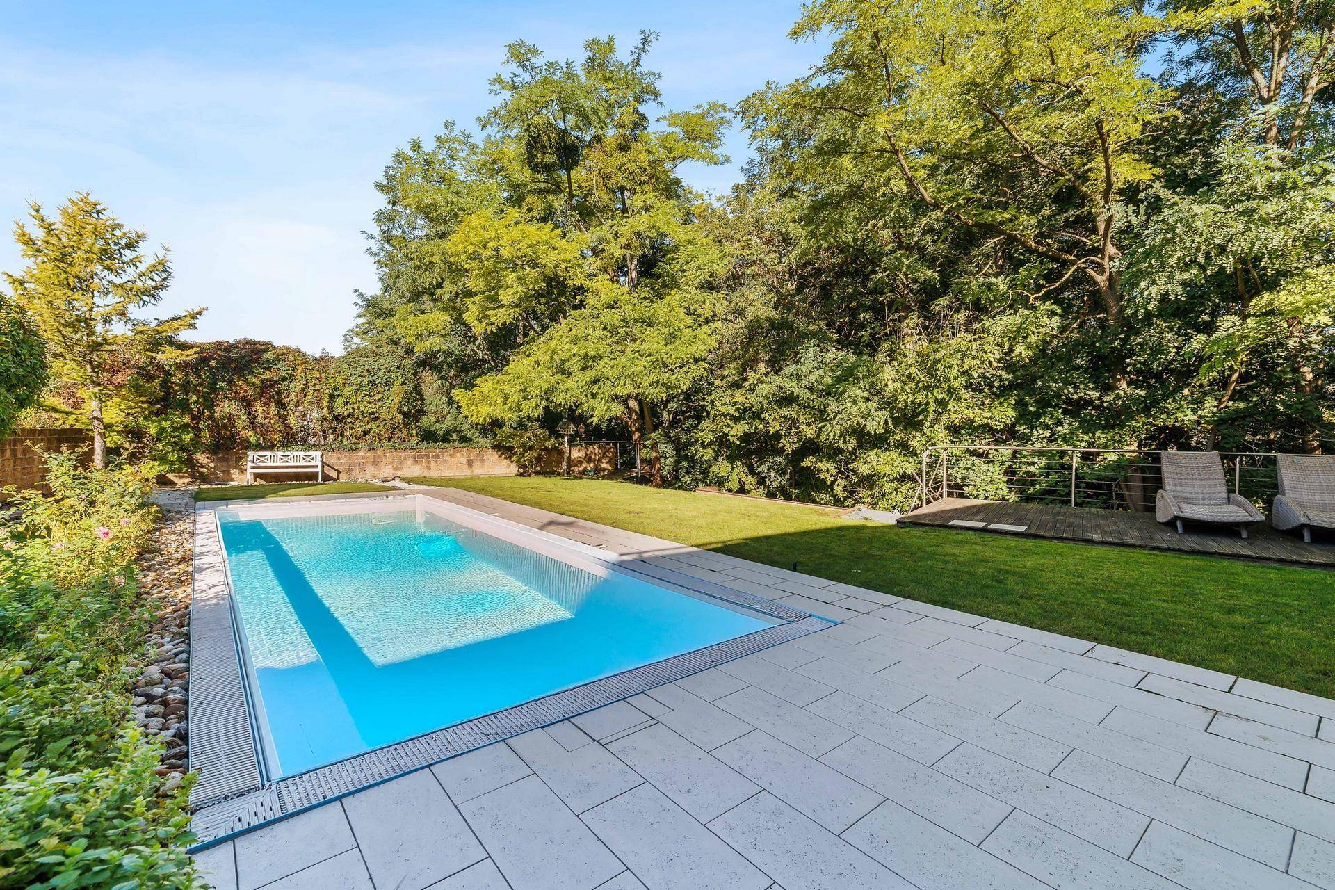 Langer Swimmingpool mit gepflasterter Umrandung und Liegeflächen im grünen Garten.