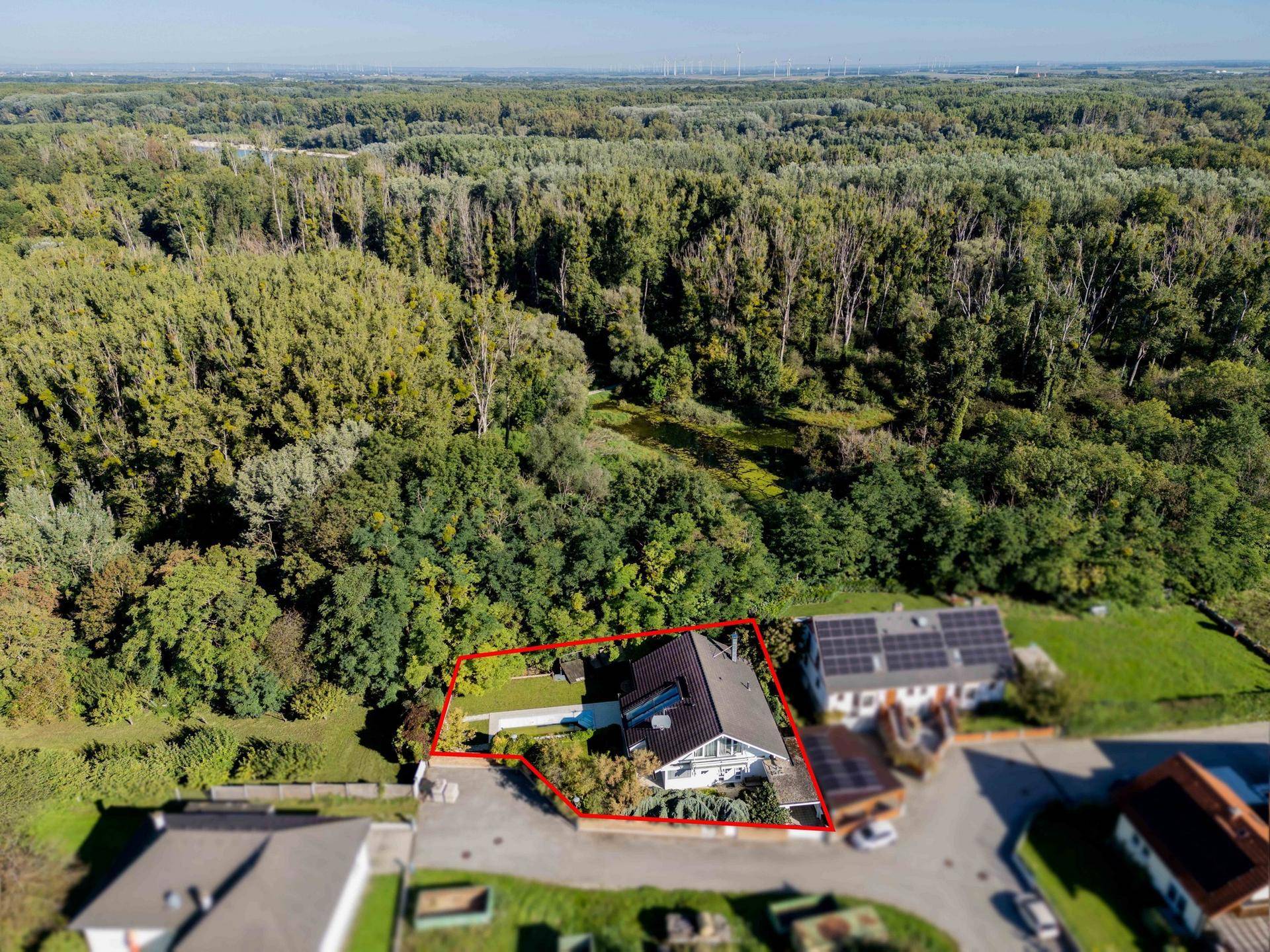 Luftaufnahme eines Hauses mit Solaranlage, umgeben von viel Grün und Wald in ländlicher Umgebung.