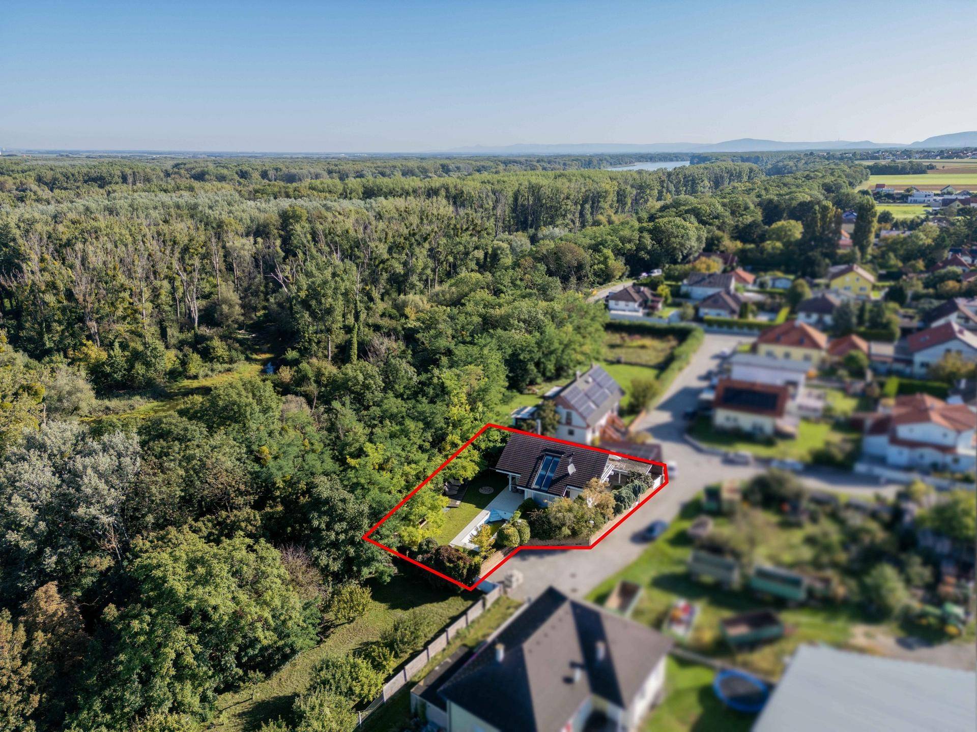 Weitläufige Luftaufnahme des Hauses mit Grundstück, umgeben von Natur und einer Siedlung am Fluss.