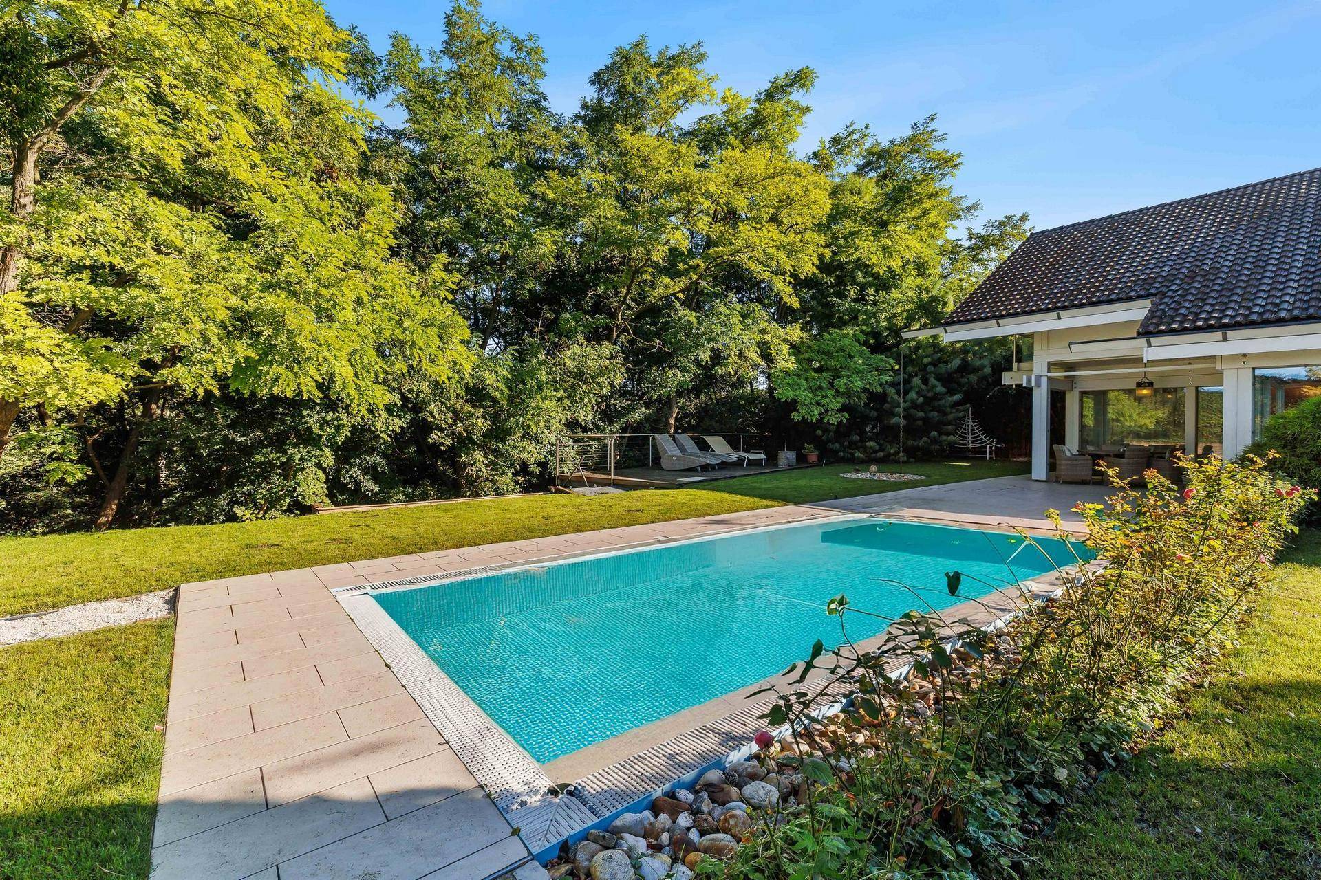 Gepflegter Garten mit überdachtem Pool und viel Grün, ideal für Entspannung im Freien.