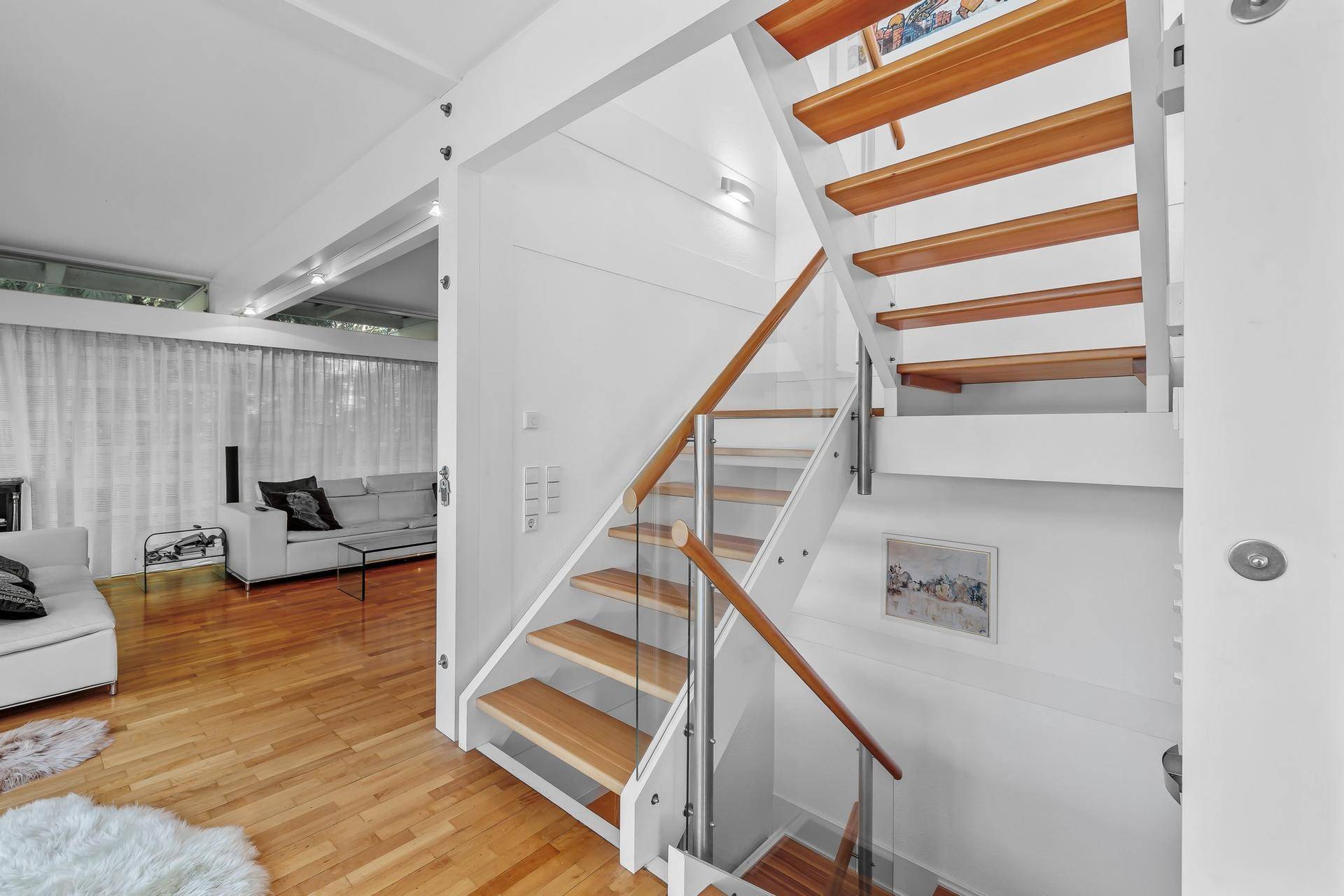 Moderne Treppe mit Holzstufen und Glasgeländer, die den Wohnbereich mit der oberen Etage verbindet.