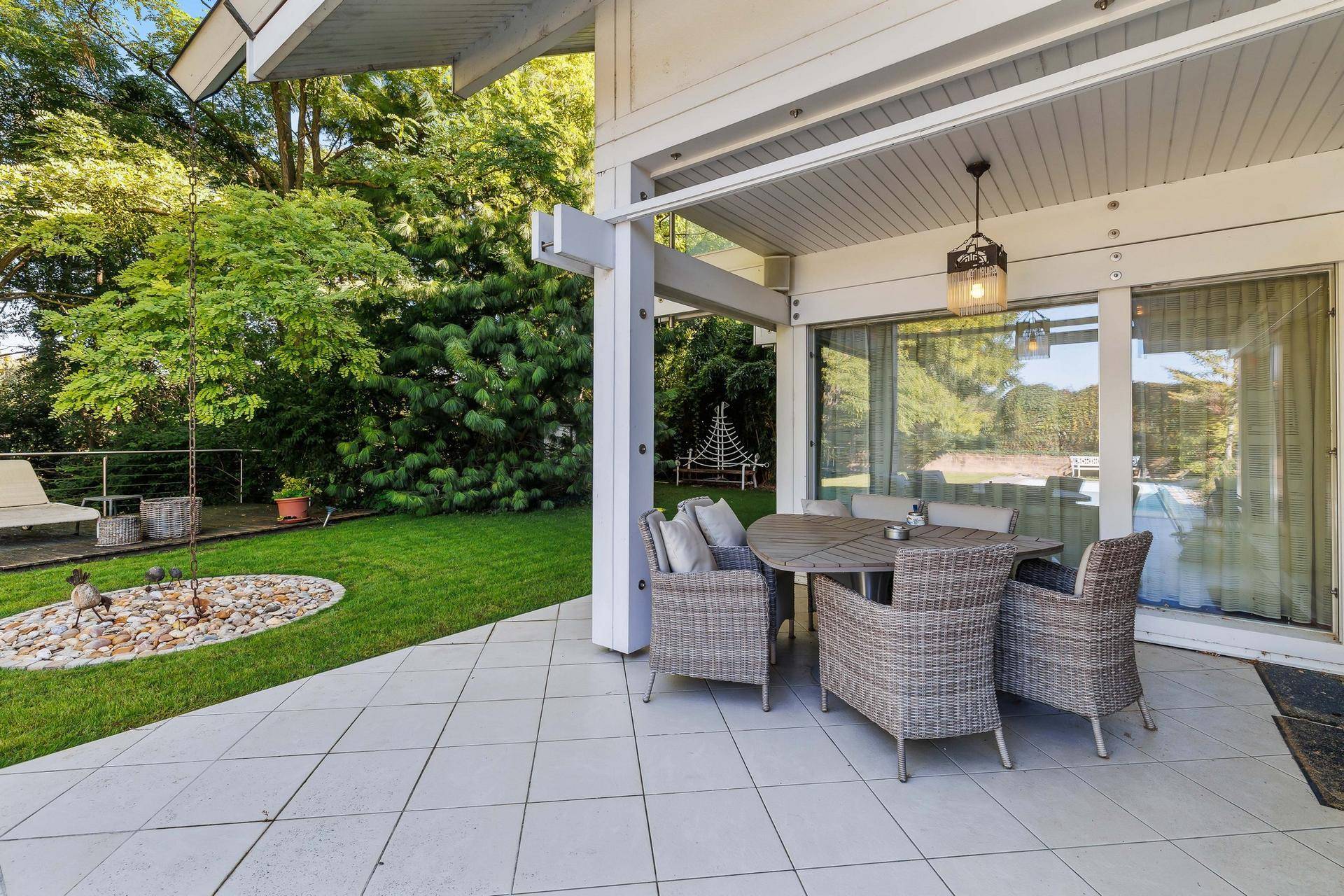 Überdachte Terrasse mit Rattanmöbeln und Esstisch, direktem Zugang zum Garten.