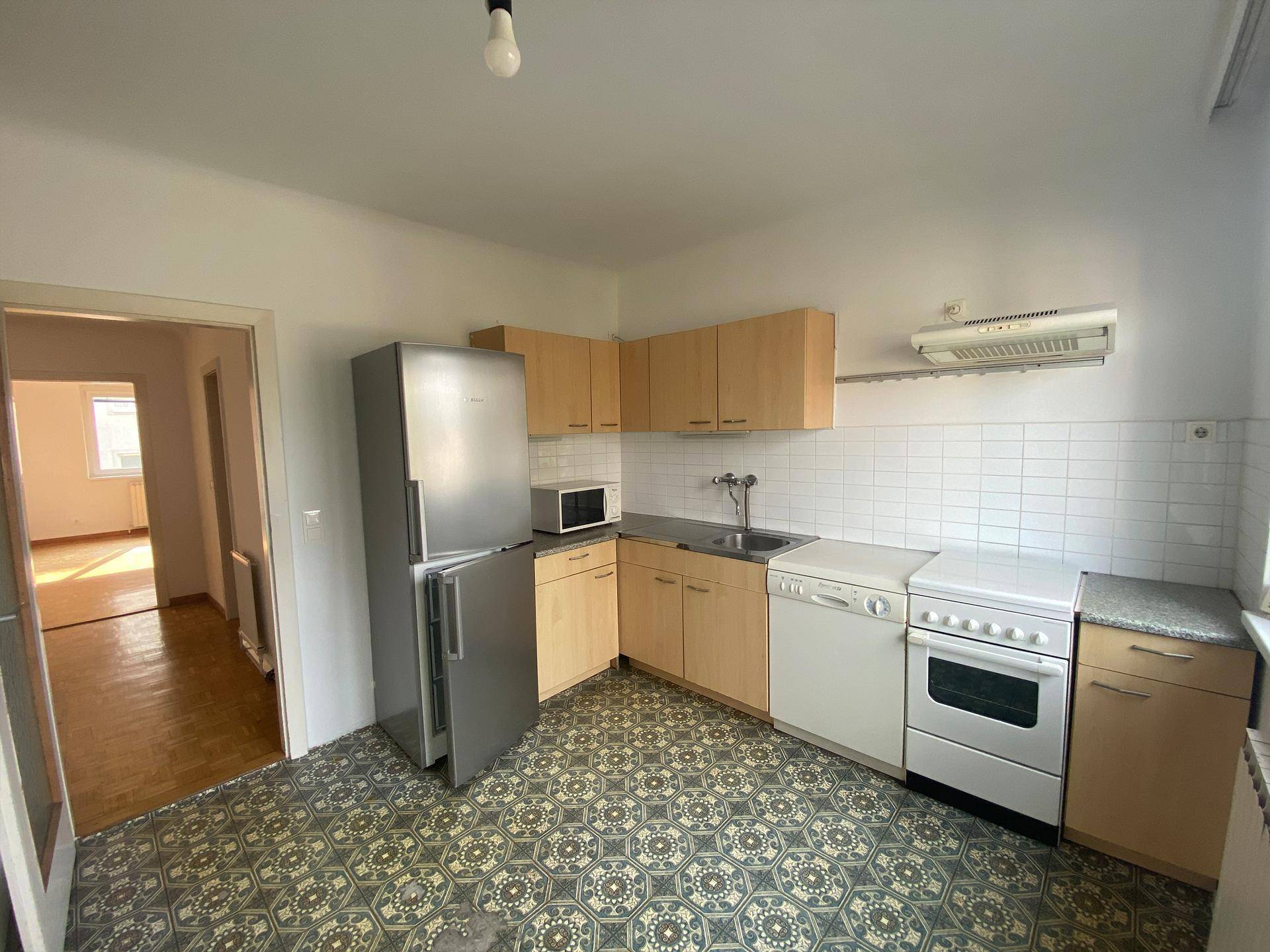 Einfache Küche mit Holzschränken, Kühlschrank, Herd und Spülmaschine.