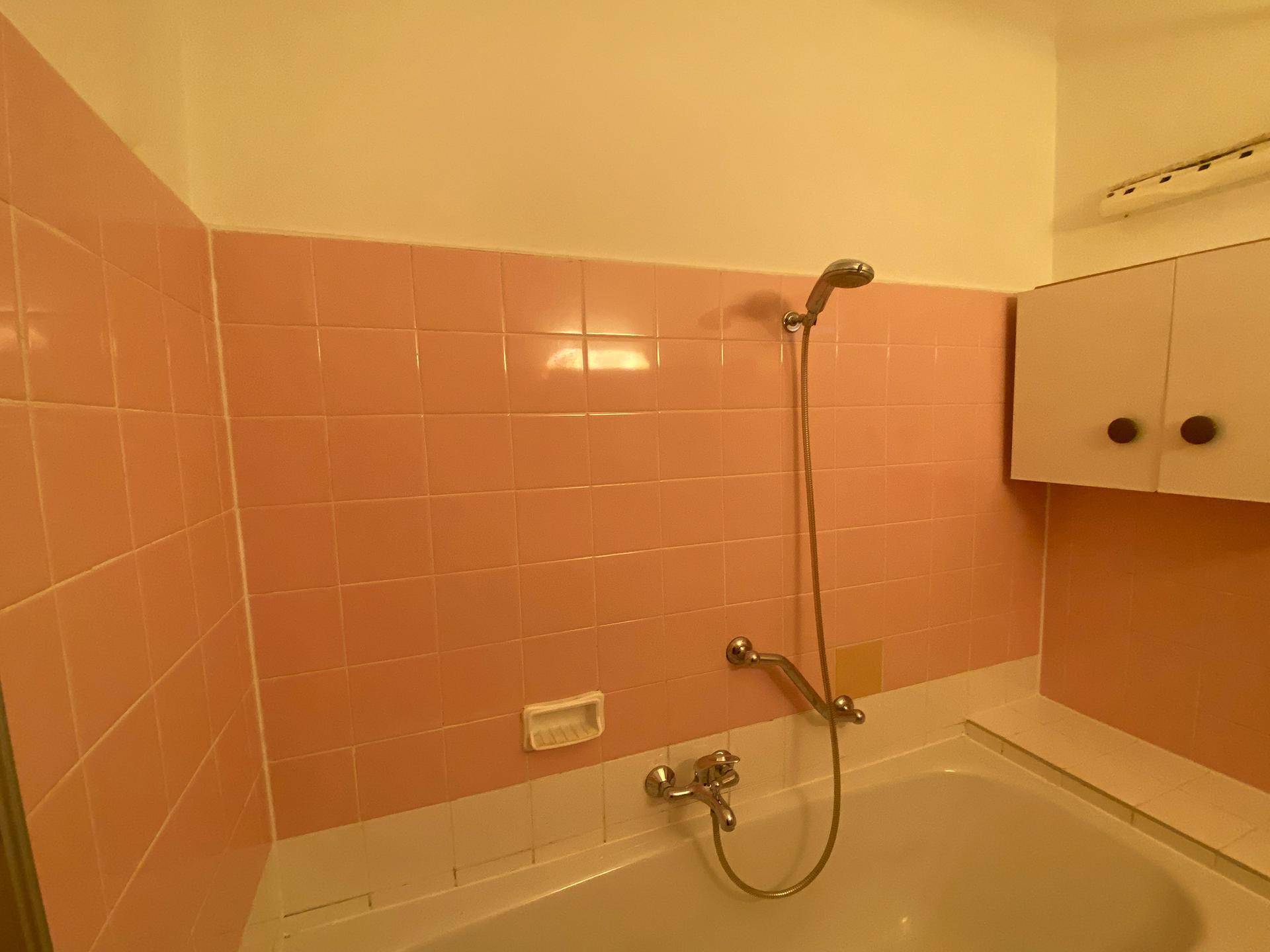 Badezimmer mit rosa Fliesen, Badewanne und Duschvorrichtung, im Stil der 80er Jahre.