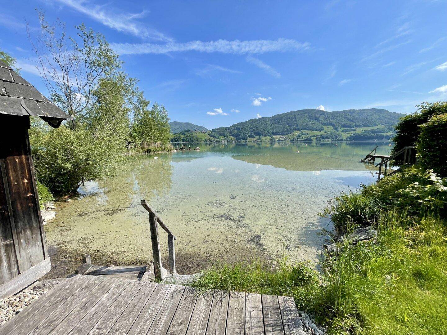 Klarer Seezugang über eine Holztreppe vom Ufer aus mit Panoramablick auf die umliegenden Berge.