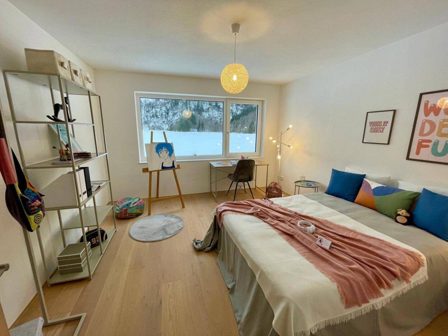 Helles Schlafzimmer mit Holzboden, Schreibtisch und Blick auf die verschneite Landschaft.