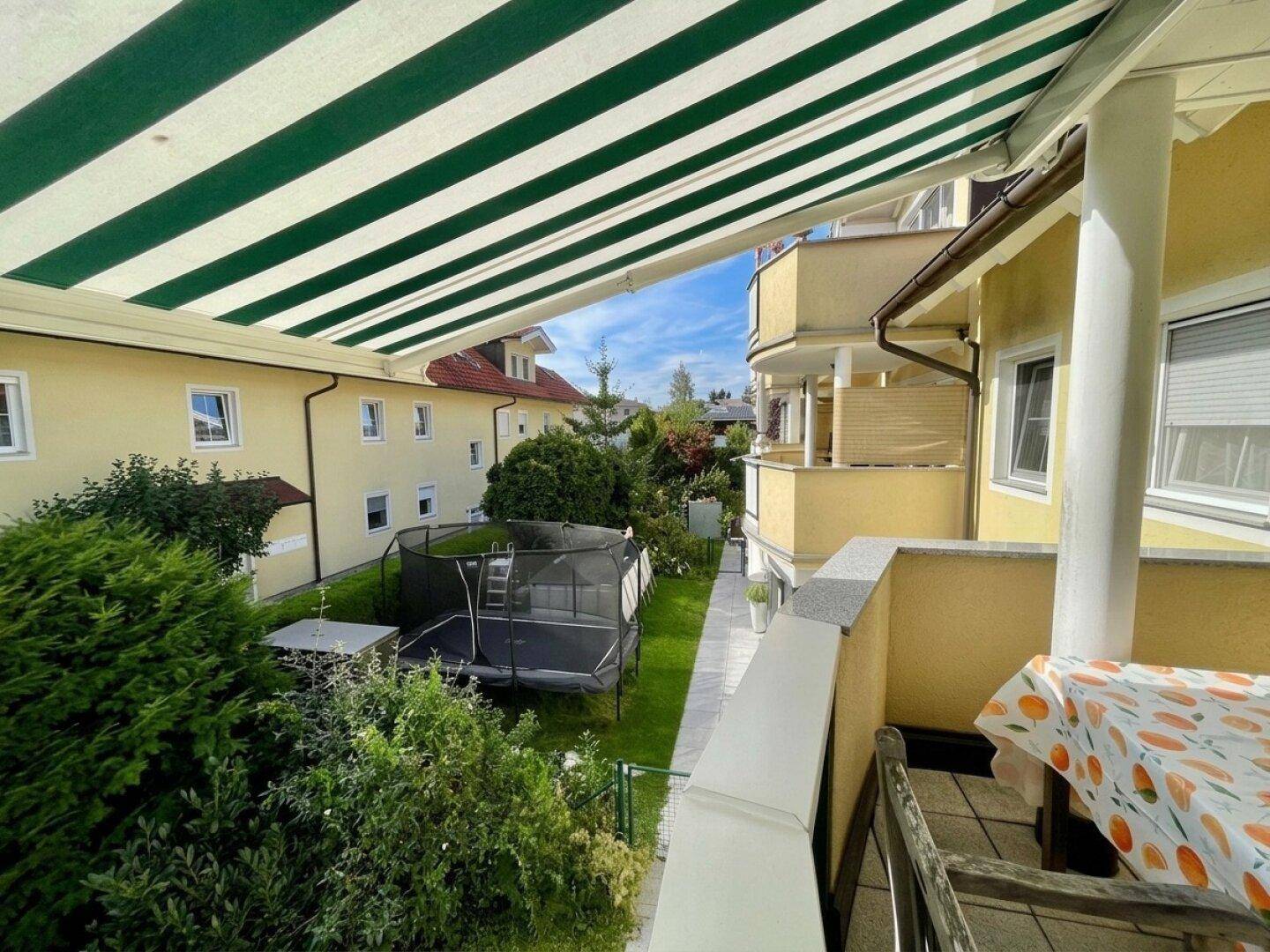 Balkon mit Markise und Blick auf den Garten mit Rasenfläche und Trampolin.